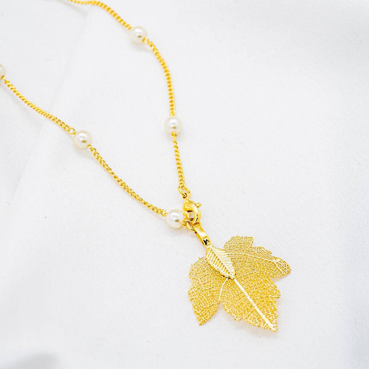 Long gold necklace with small round white pearls and openwork gold leaf pendant