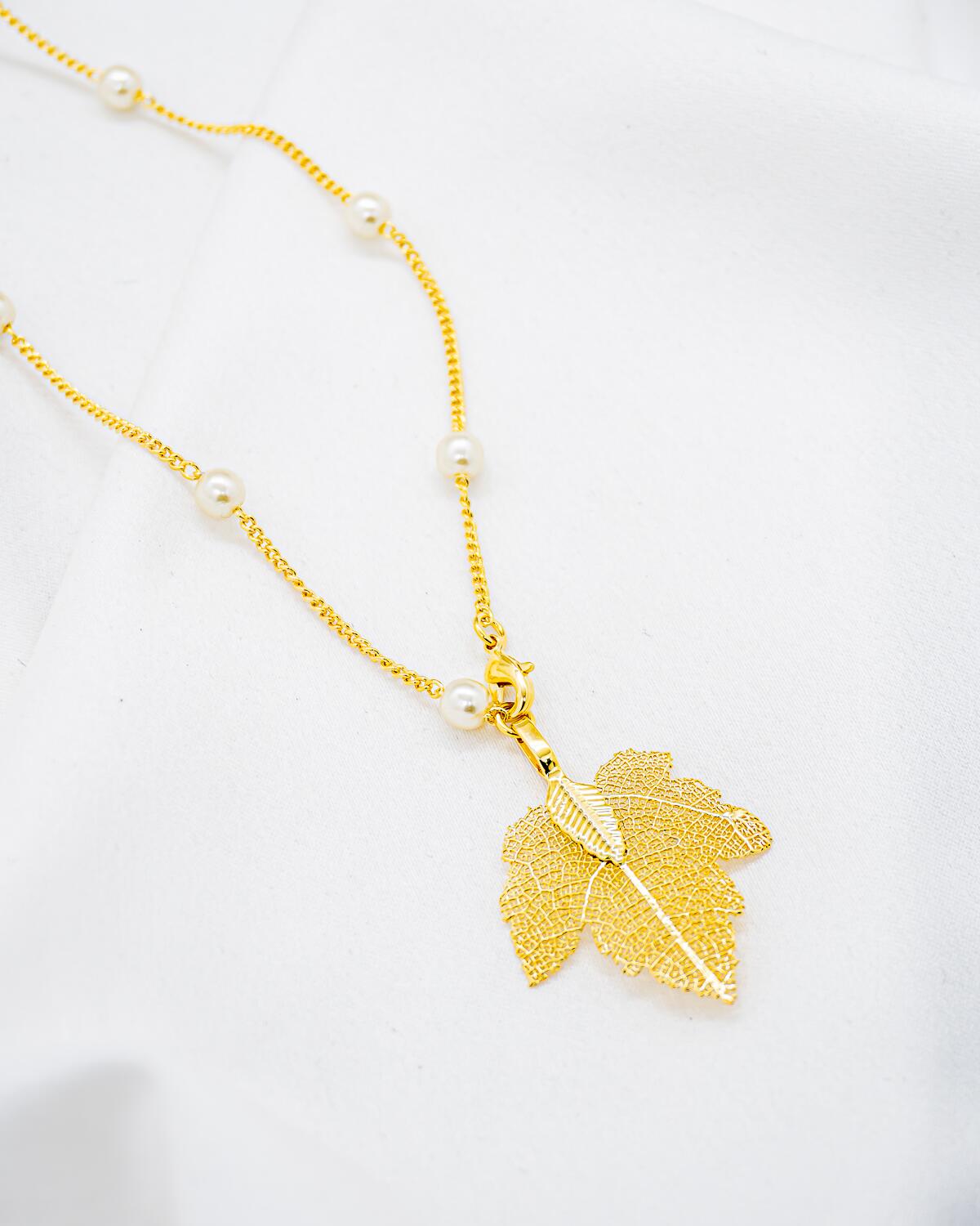 Collier long doré avec petites perles blanches rondes et pendentif feuille dorée ajourée