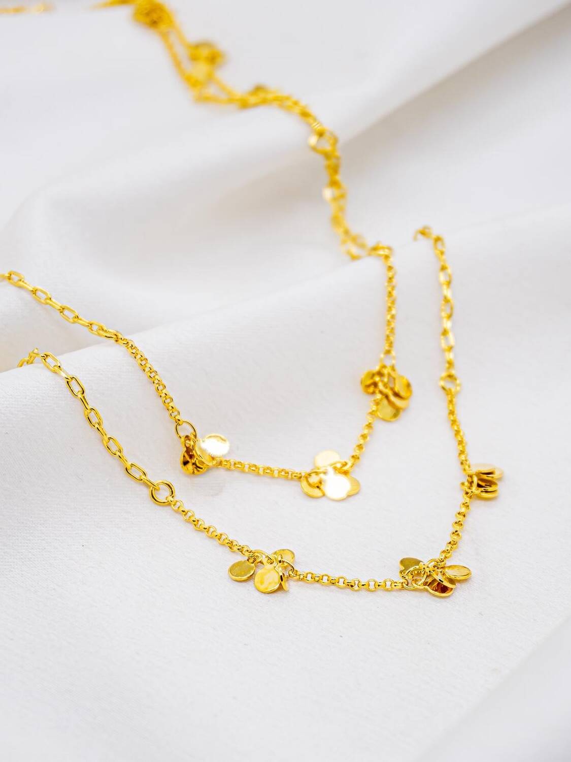 Collier long doré, petits groupes de disques lisses sur chaîne fine, posé sur tissu
