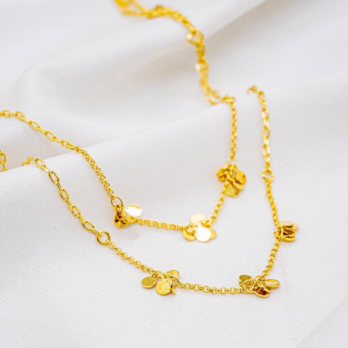 Long gold necklace, small clusters of smooth discs on fine chain, laid on fabric
