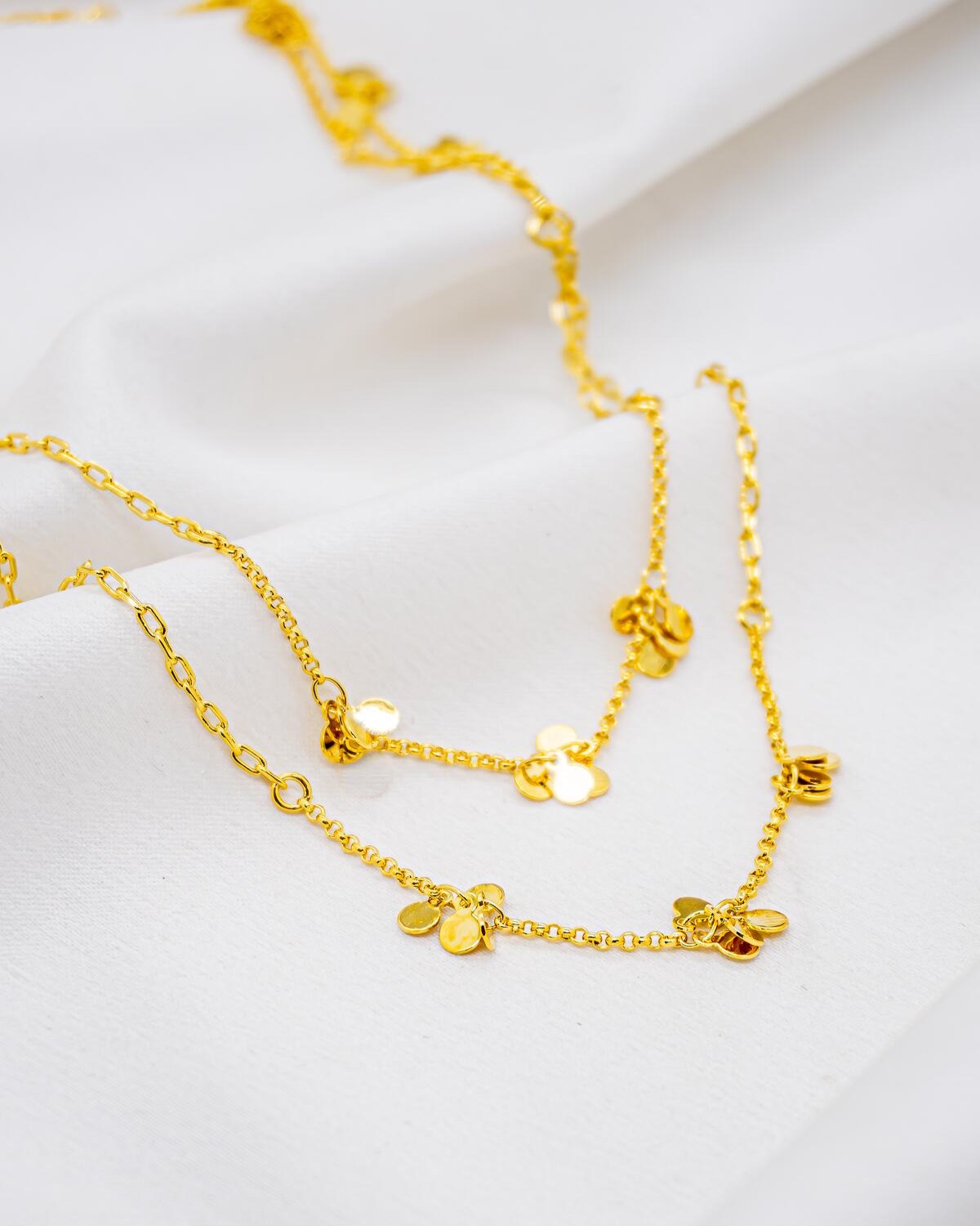Long gold necklace, small clusters of smooth discs on fine chain, laid on fabric