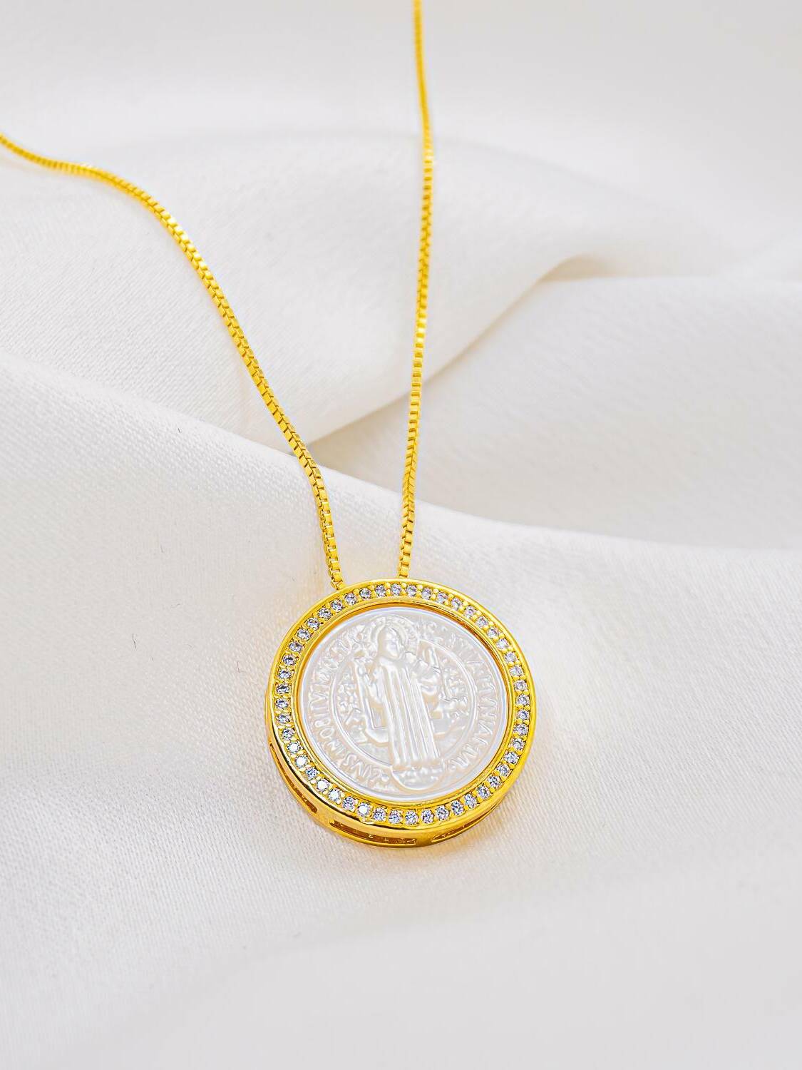 Pendentif rond en nacre avec médaille de Saint Benoît gravée, bordure de pierres claires, chaîne dorée