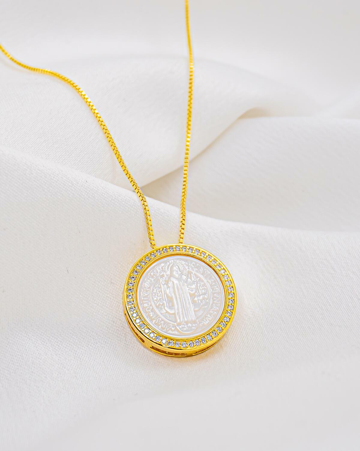 Pendentif rond en nacre avec médaille de Saint Benoît gravée, bordure de pierres claires, chaîne dorée