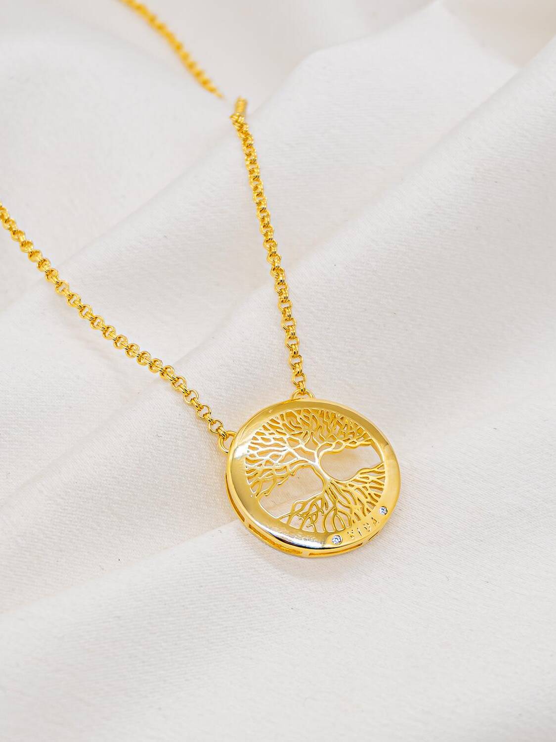 Collier doré à pendentif rond ajouré représentant un arbre de vie, avec deux petites pierres claires