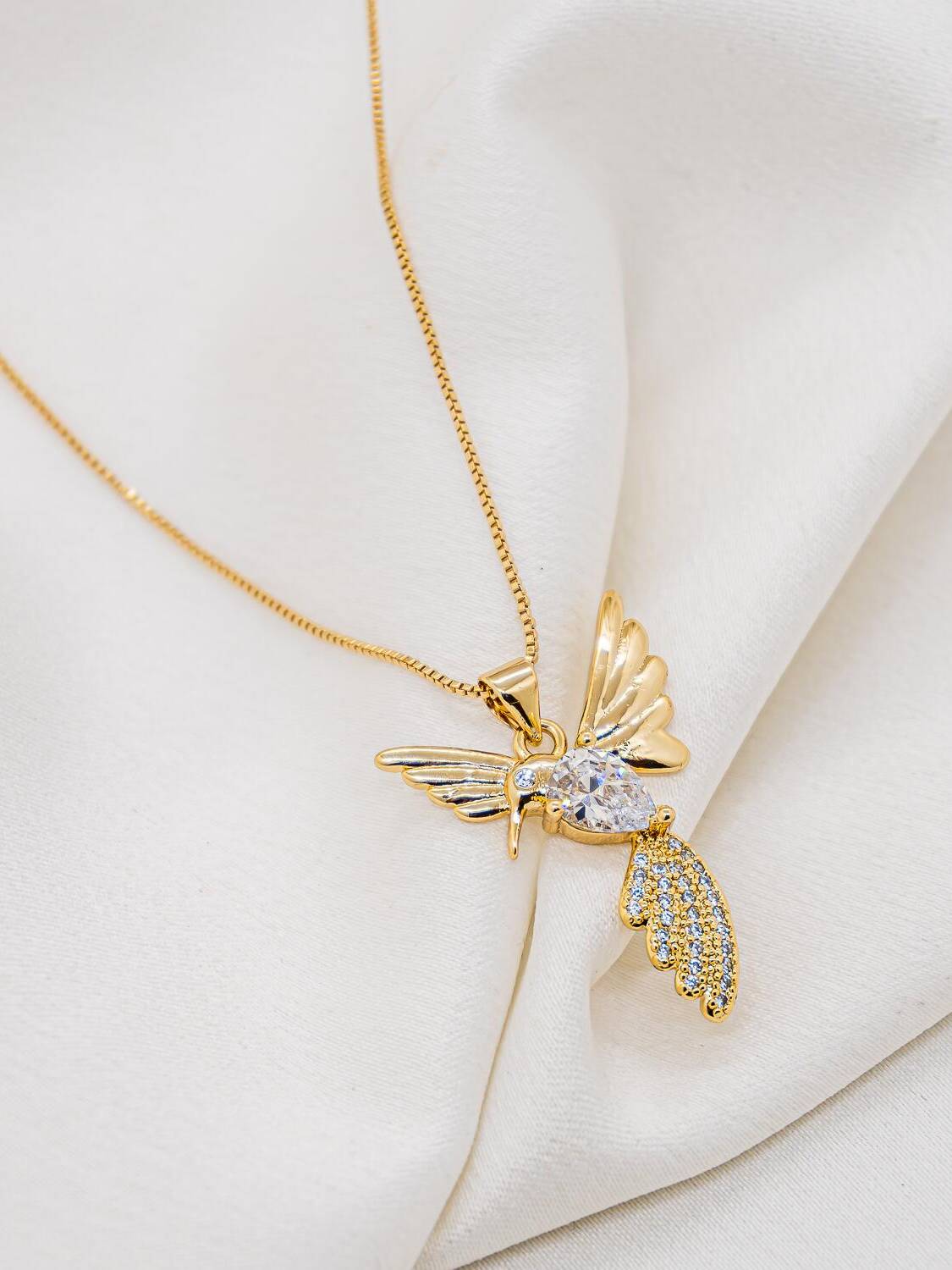Collier doré à fine chaîne et pendentif colibri aux ailes déployées, pierre claire en goutte