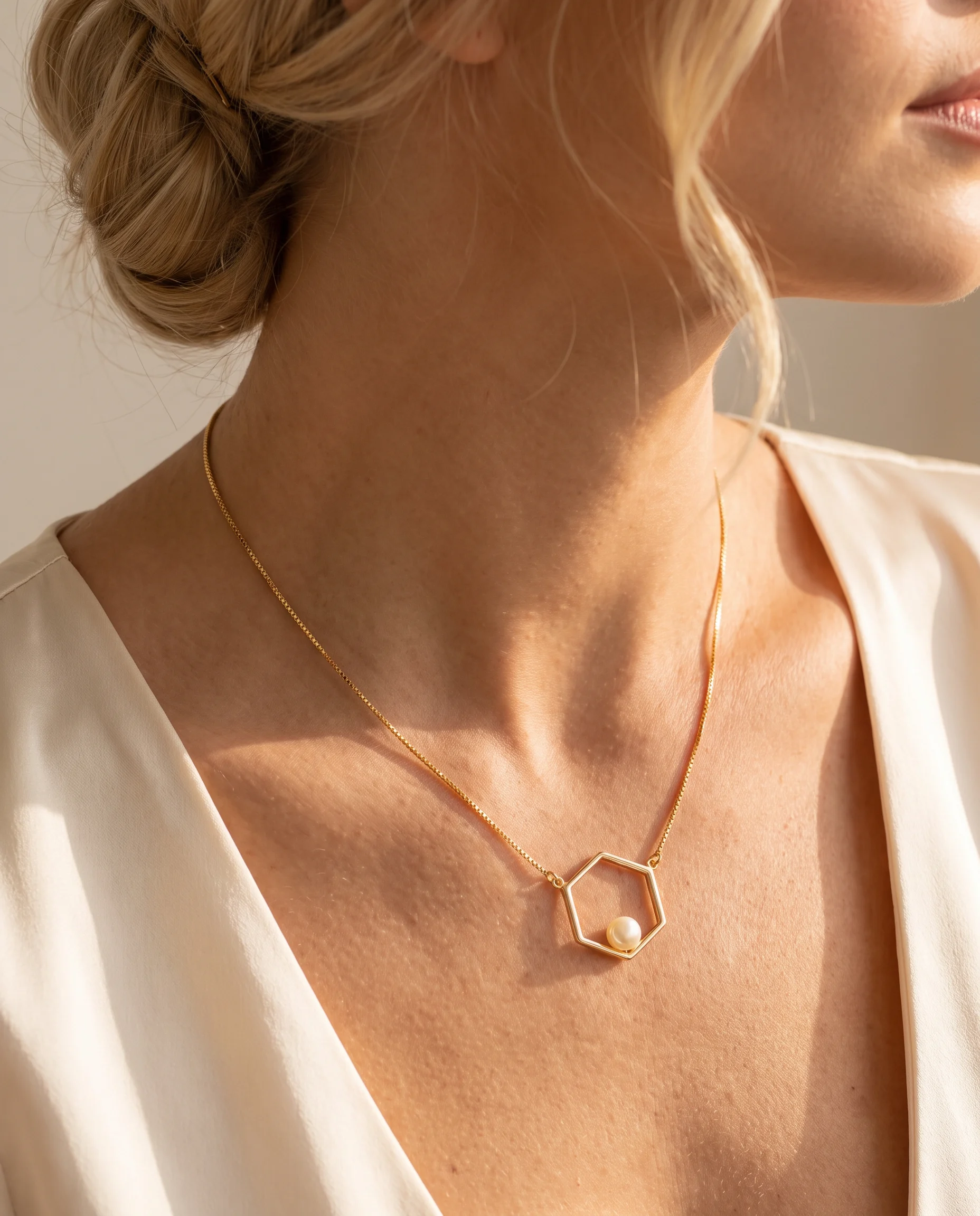 Collier doré à pendentif hexagone ajouré et petite perle blanche, vu de près