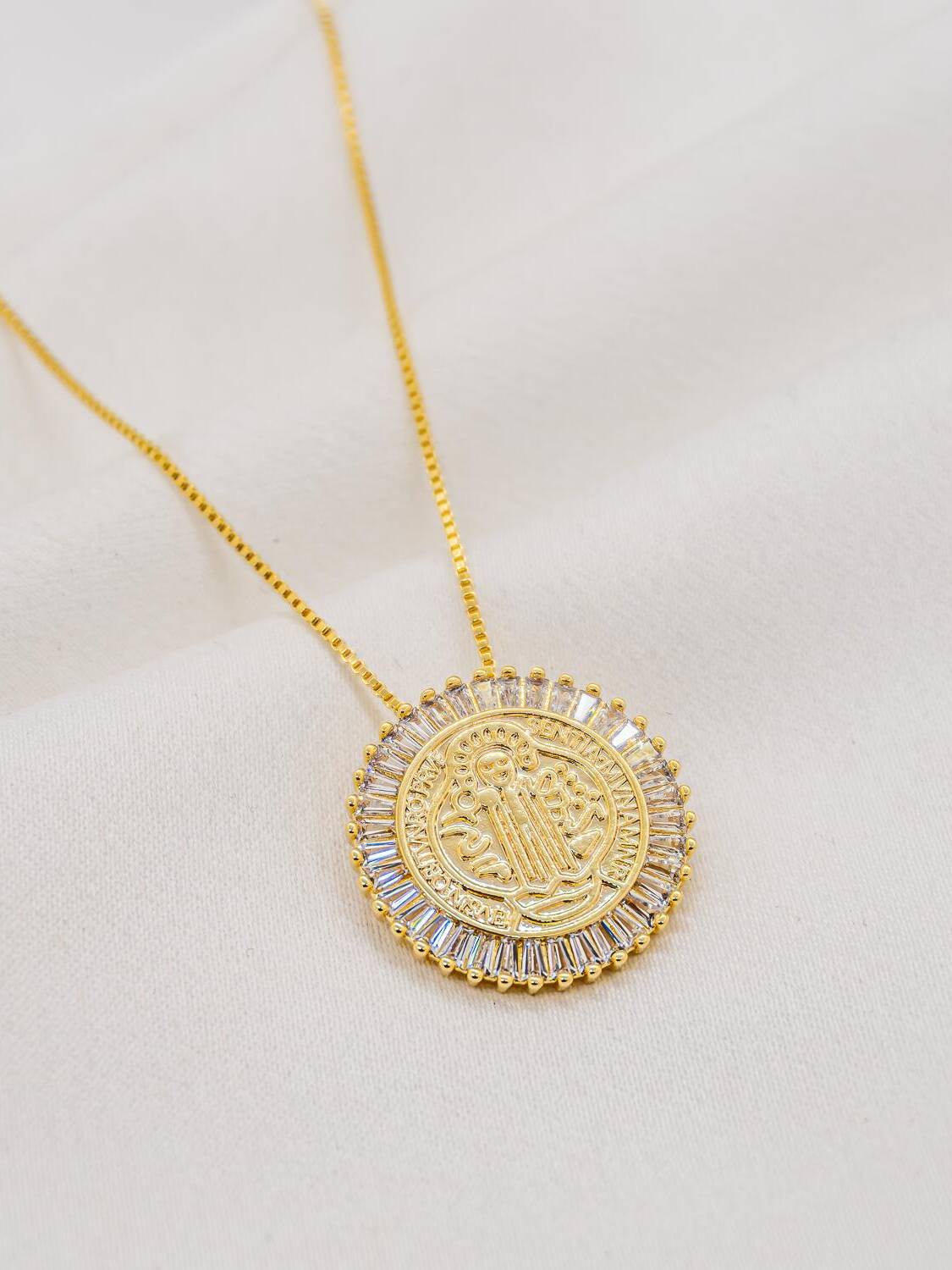 Collier doré à médaille ronde gravée entourée de pierres claires en baguettes