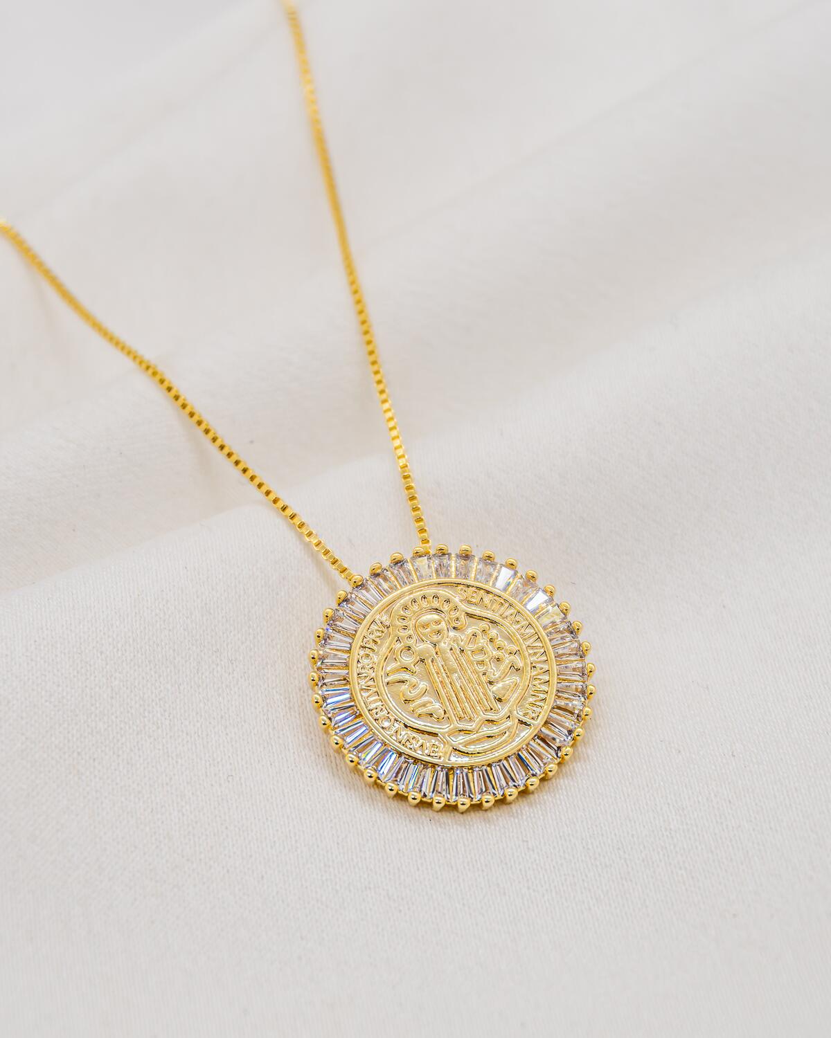 Colar dourado com medalha redonda gravada cercada por zircônias incolores baguete
