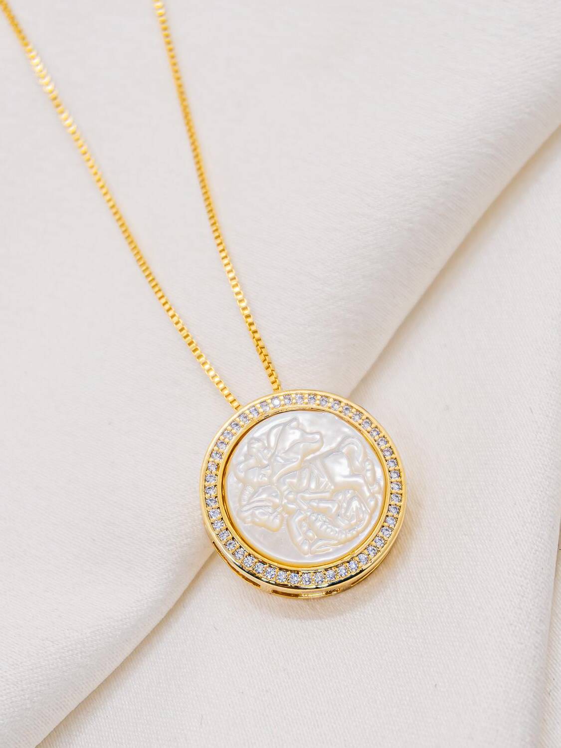 Collier doré à médaille ronde de nacre blanche cerclée de pierres claires