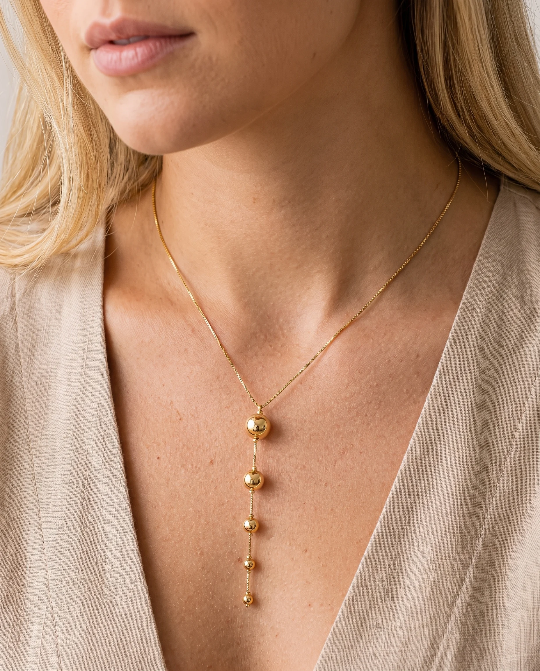 Gold necklace with cascading smooth, decreasing spheres, worn on the chest, close-up view