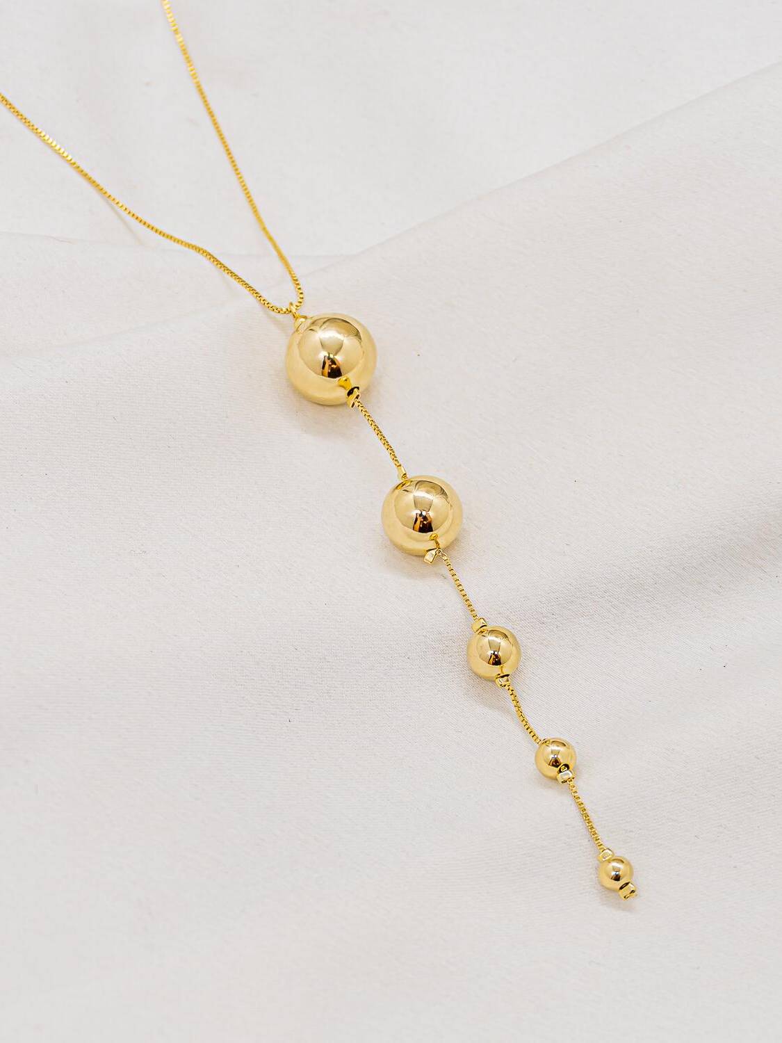 Collier doré à fine chaîne, longue chute de sphères lisses et brillantes de taille décroissante