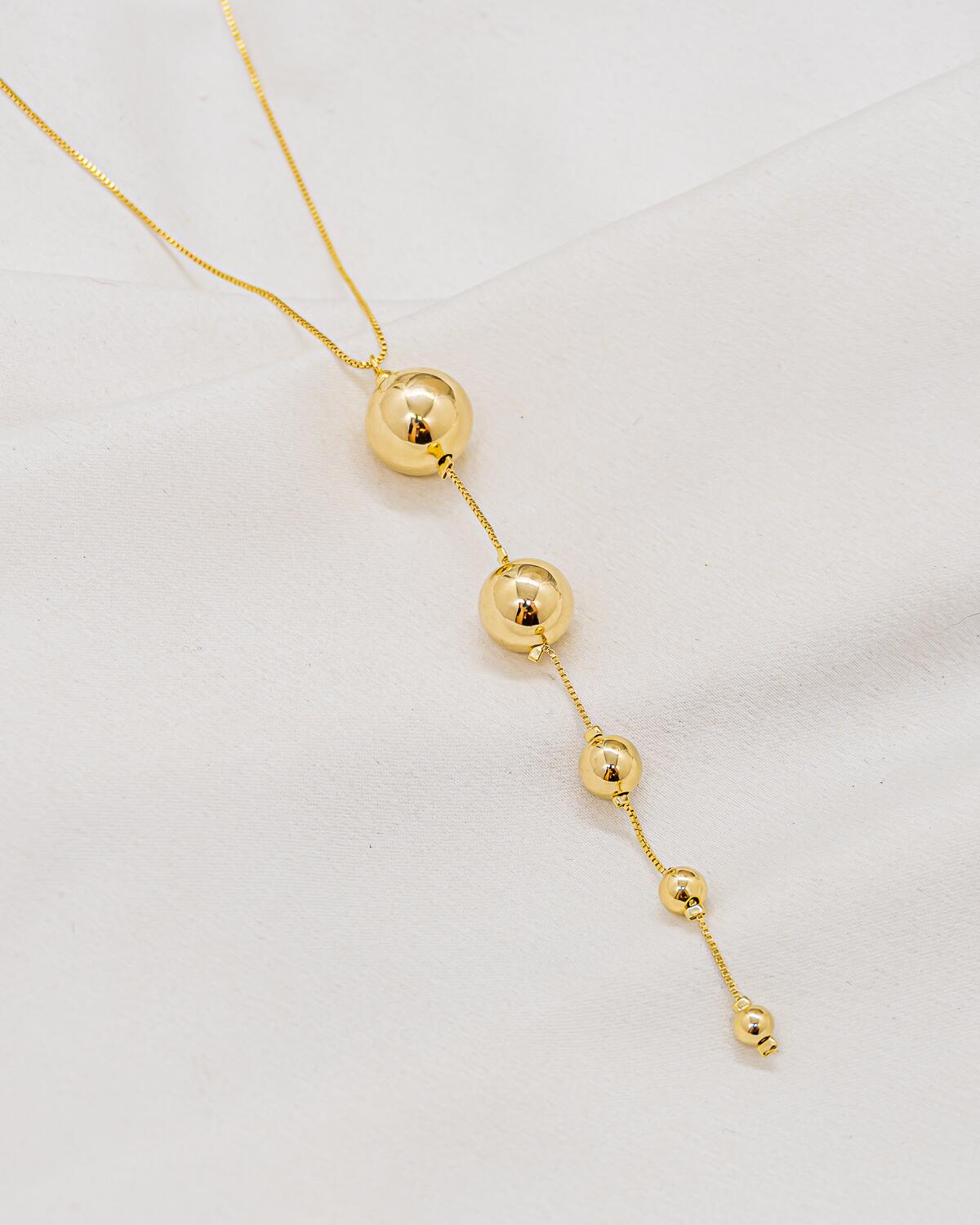 Gold necklace with a fine chain, long cascade of smooth, shiny spheres in decreasing size