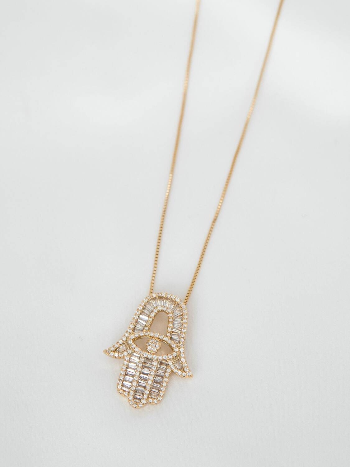 Pendentif main de Fatima ajouré orné de pierres claires baguettes et rondes, sur fine chaîne dorée