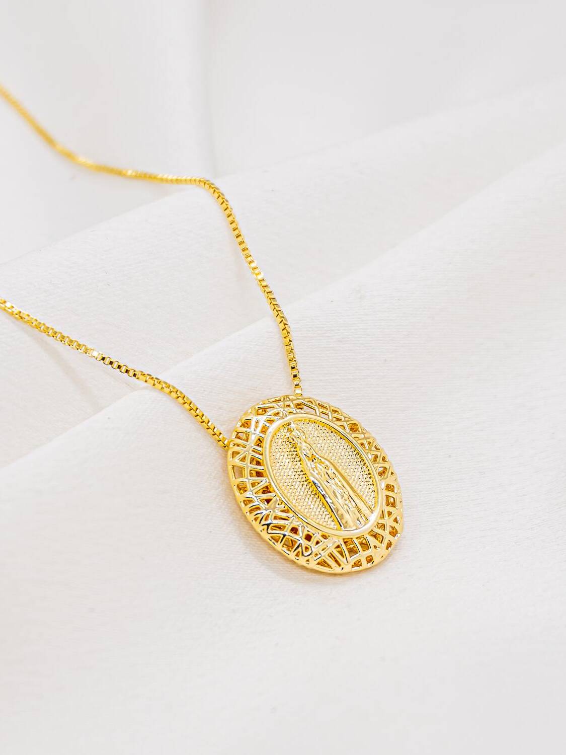 Collier doré à pendentif ovale montrant une silhouette en relief, entourée d’un cadre filigrané