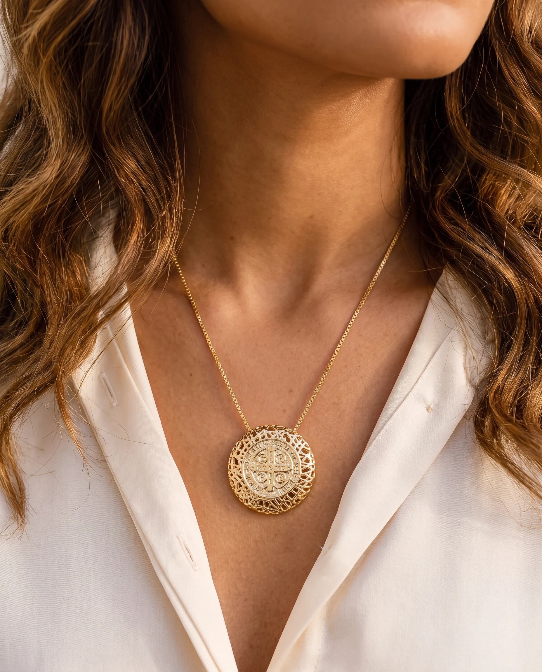 Colar dourado com medalha redonda vazada do lado da cruz, usado no peito, visto de perto