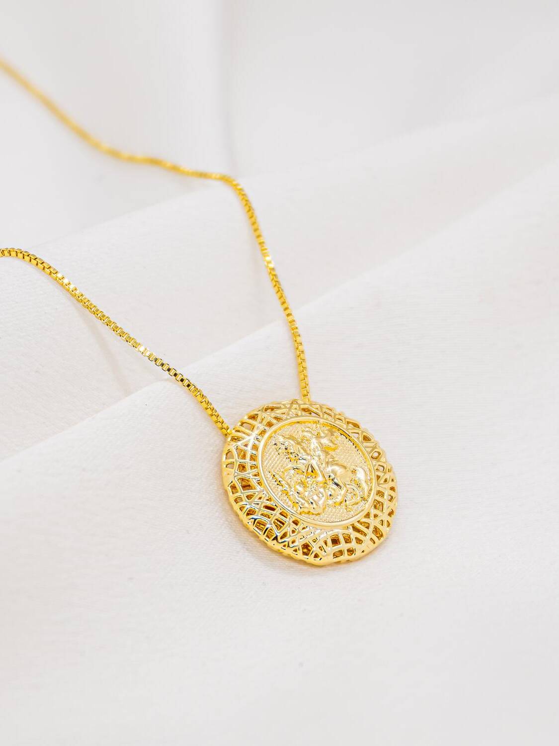 Collier doré à médaillon rond montrant un cavalier à la lance en relief, cadre filigrané