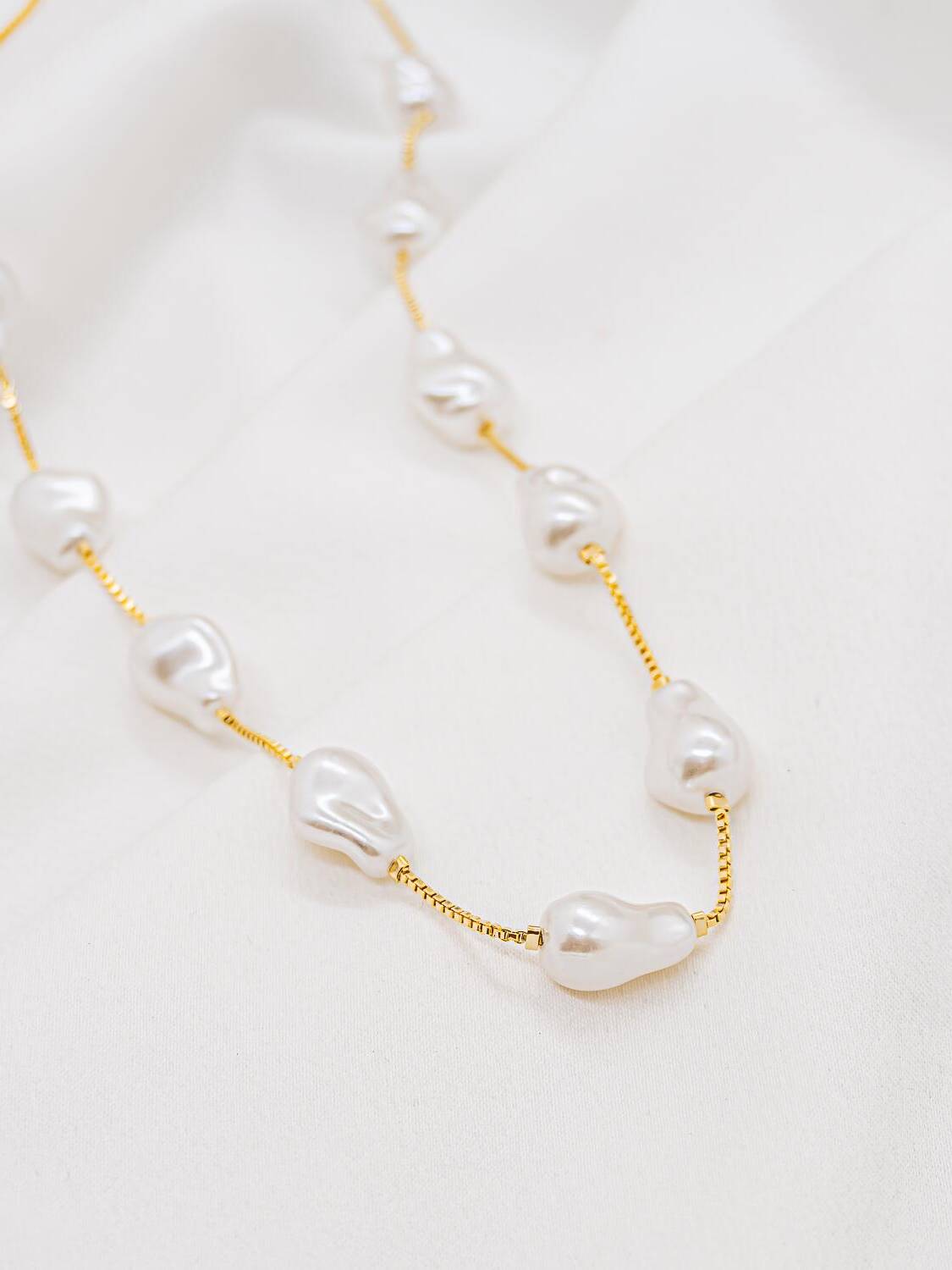 Collier doré à fine chaîne vénitienne et perles baroques blanches irrégulières, posé sur un tissu clair