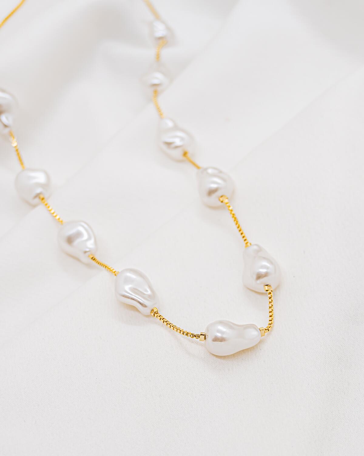 Collier doré à fine chaîne vénitienne et perles baroques blanches irrégulières, posé sur un tissu clair