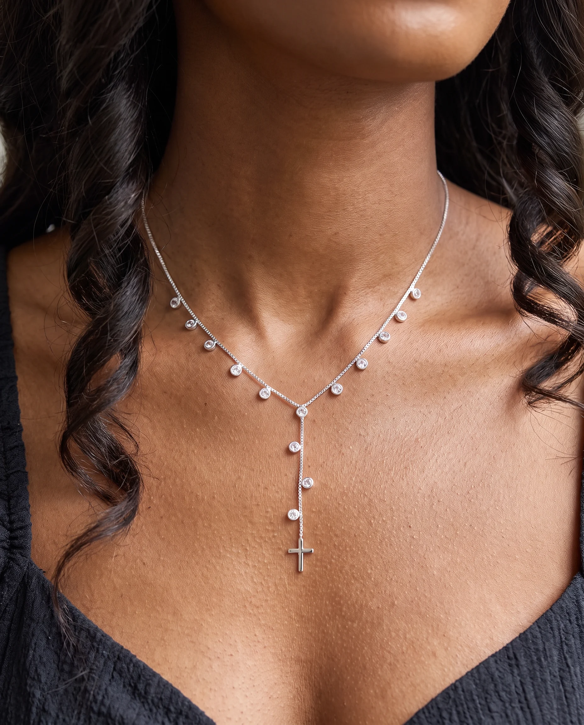 Collier argenté à pierres claires pendantes et croix lisse, porté sur la poitrine, vu de près