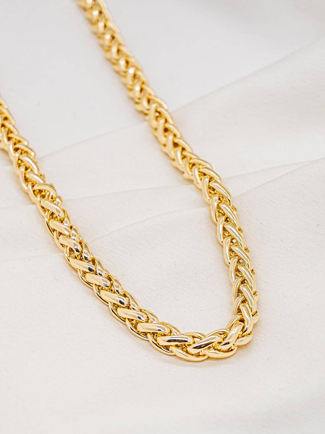 Collier doré en large maille tressée, maillons entrelacés brillants en épi, sur tissu blanc