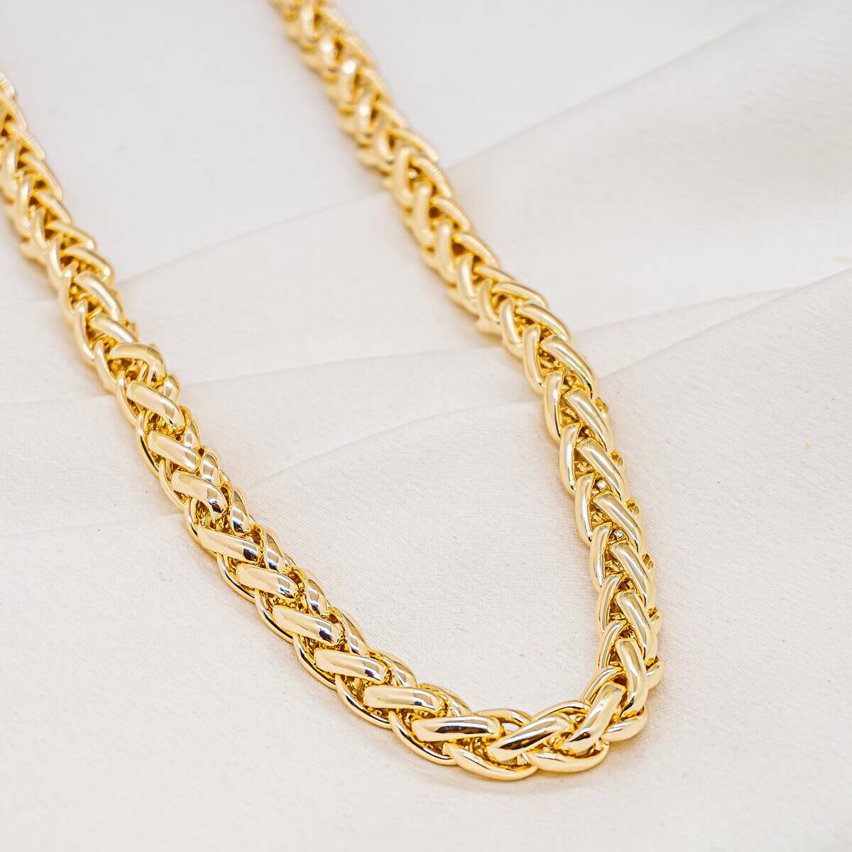 Gold necklace in wide braided chain, shiny herringbone links, on white fabric