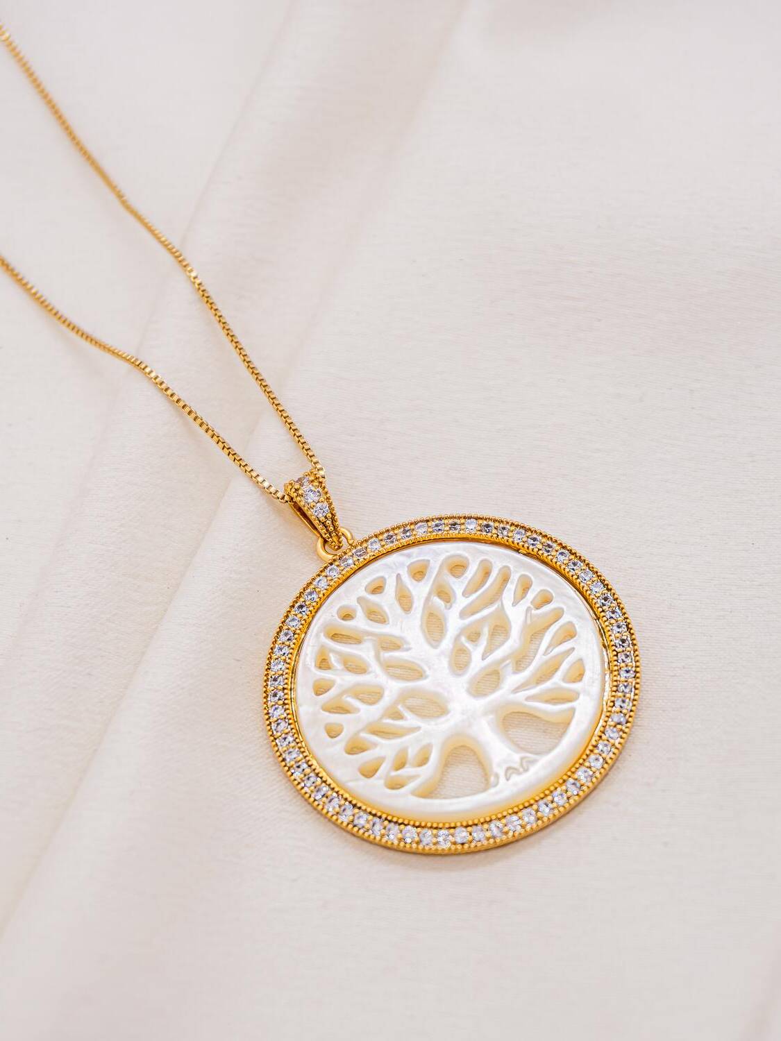 Collier doré, médaille ronde en nacre ajourée en arbre de vie, bordure de pierres claires serties