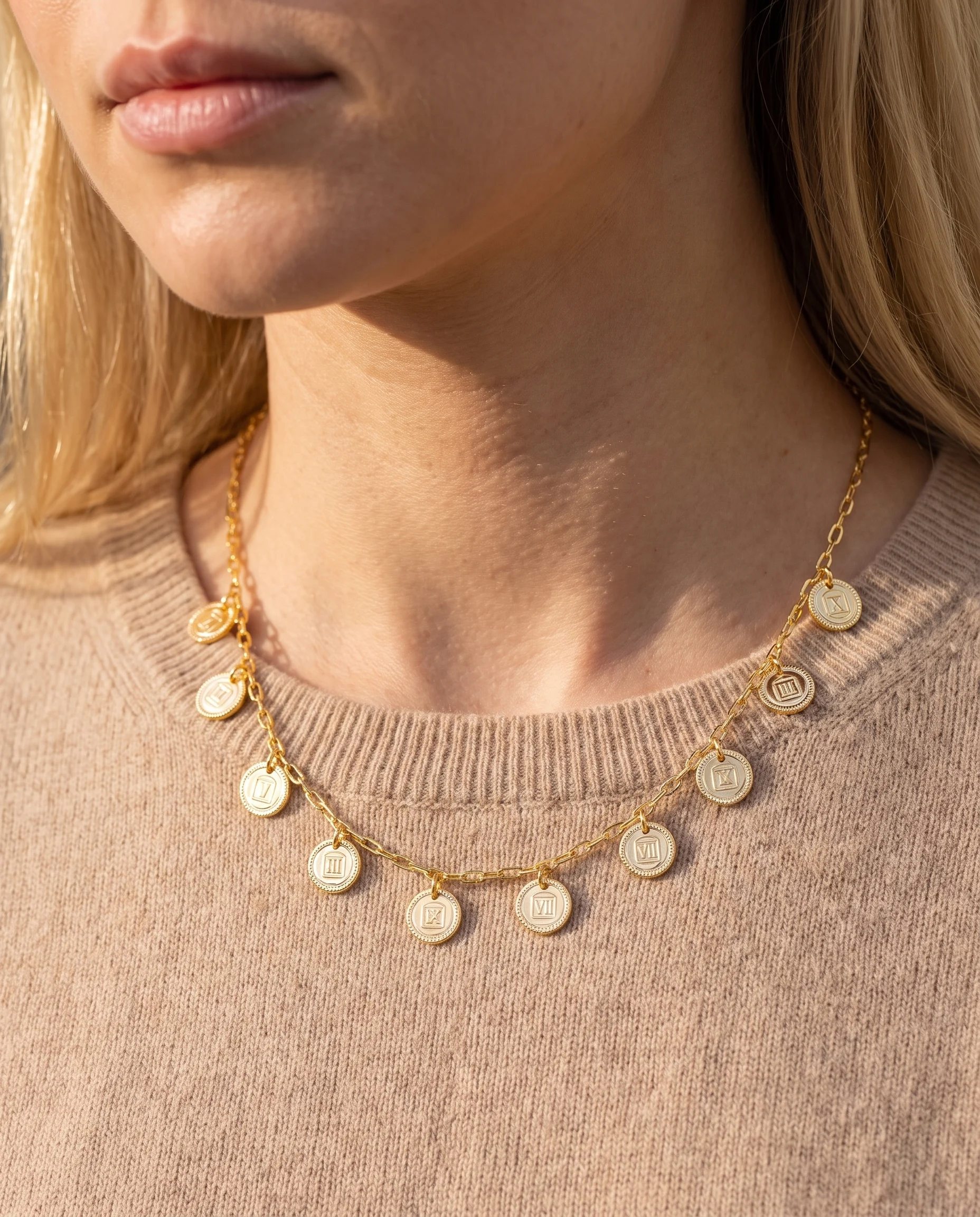 Collier doré à mini maille ovale et petites médailles gravées, porté sur les clavicules, vu de près