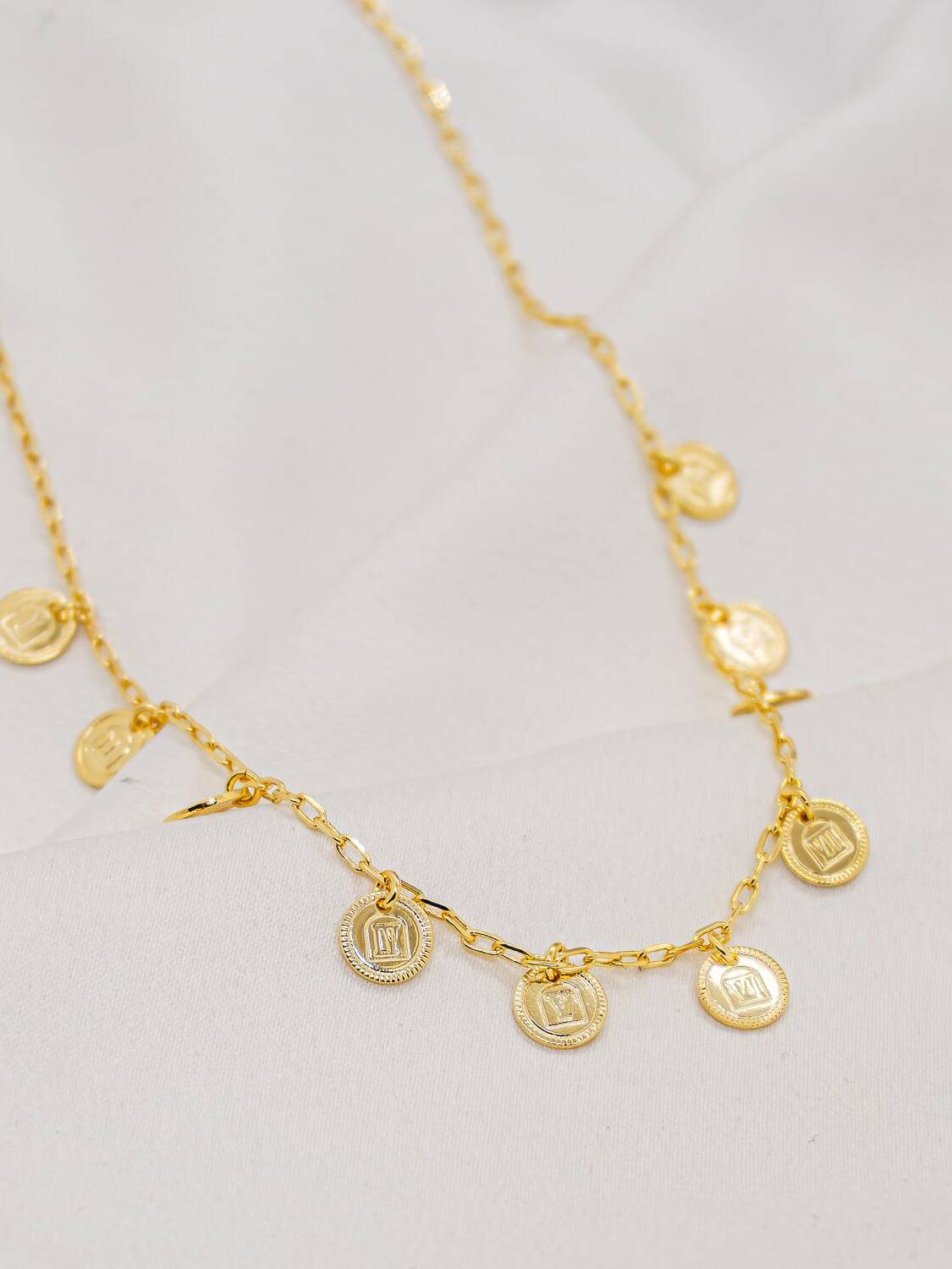 Collier doré à maillons allongés, orné de petites médailles rondes au motif carré