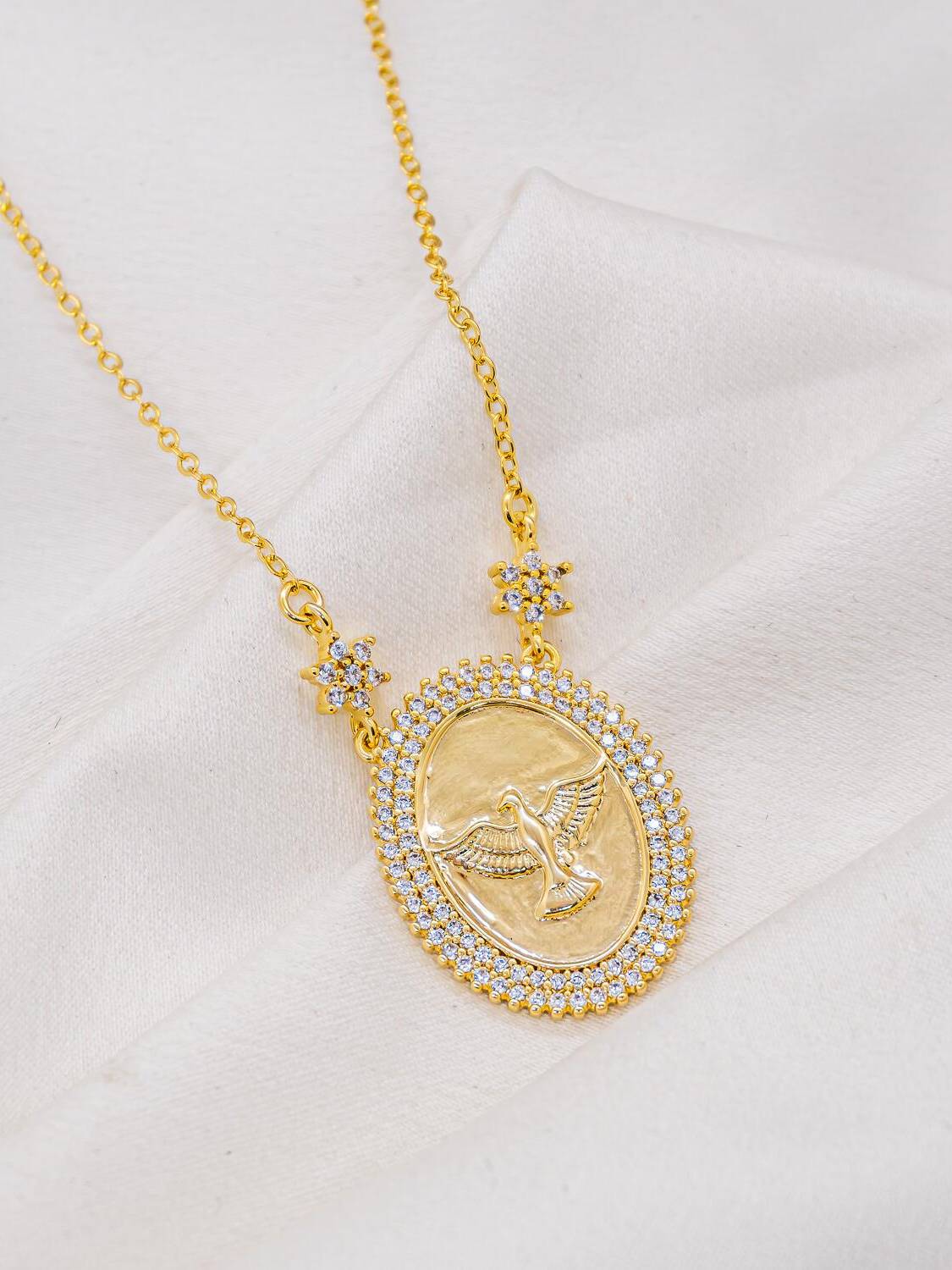 Collier doré à médaille ovale de colombe entourée de pierres claires et de deux fleurs serties