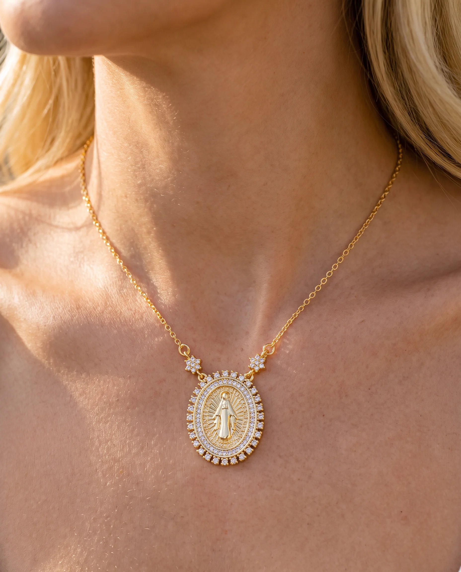 Collier doré à médaille ovale de la Vierge cernée de pierres claires, vu de près