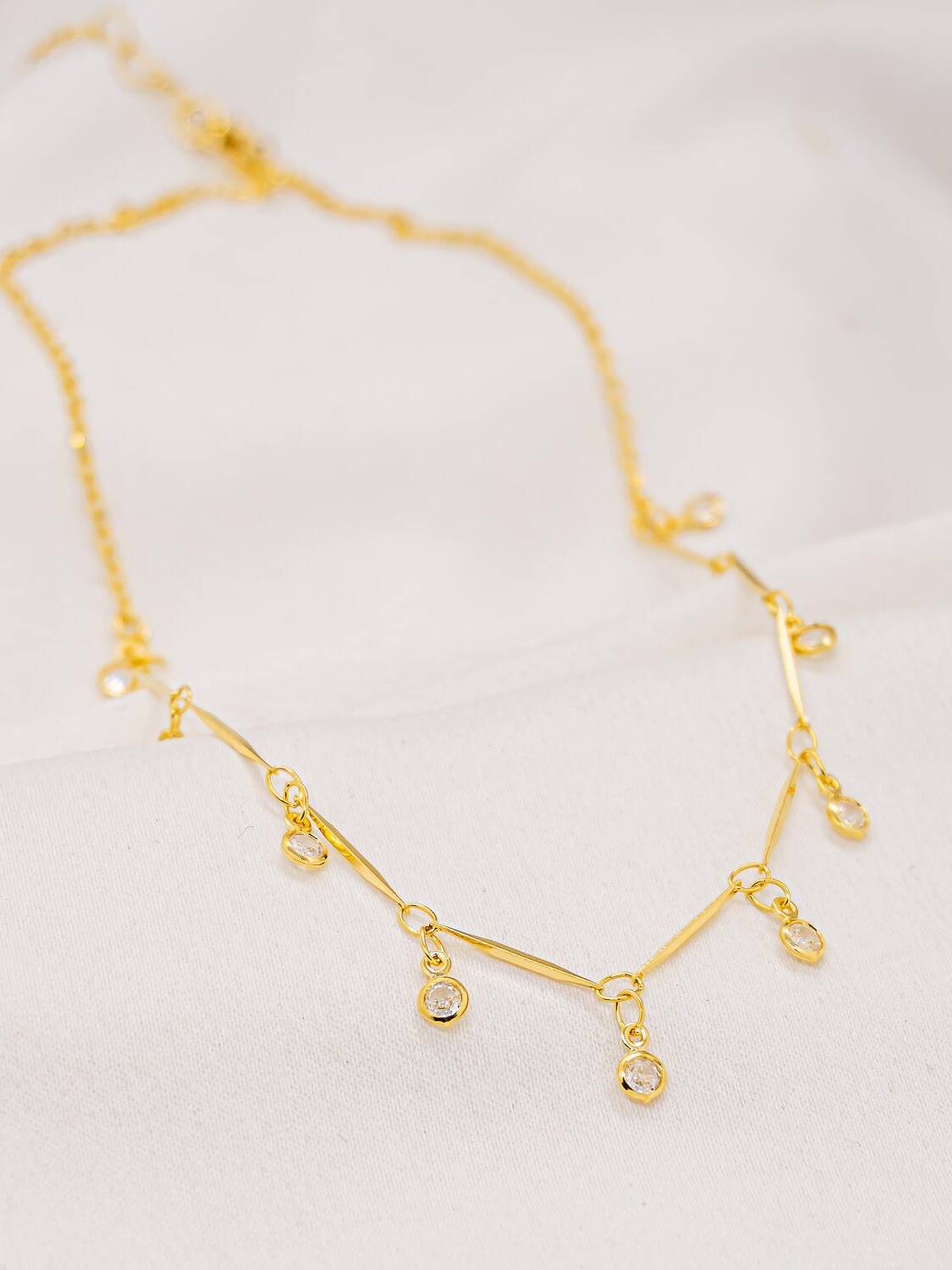 Collier doré en chaîne fine à petits bâtonnets, avec pierres claires serties qui pendent