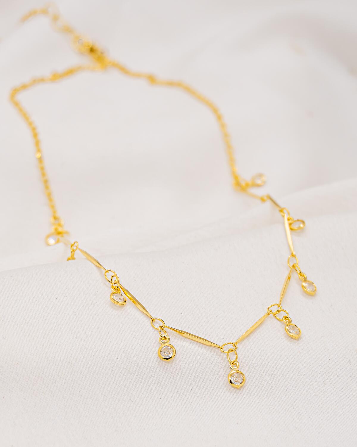 Collier doré en chaîne fine à petits bâtonnets, avec pierres claires serties qui pendent