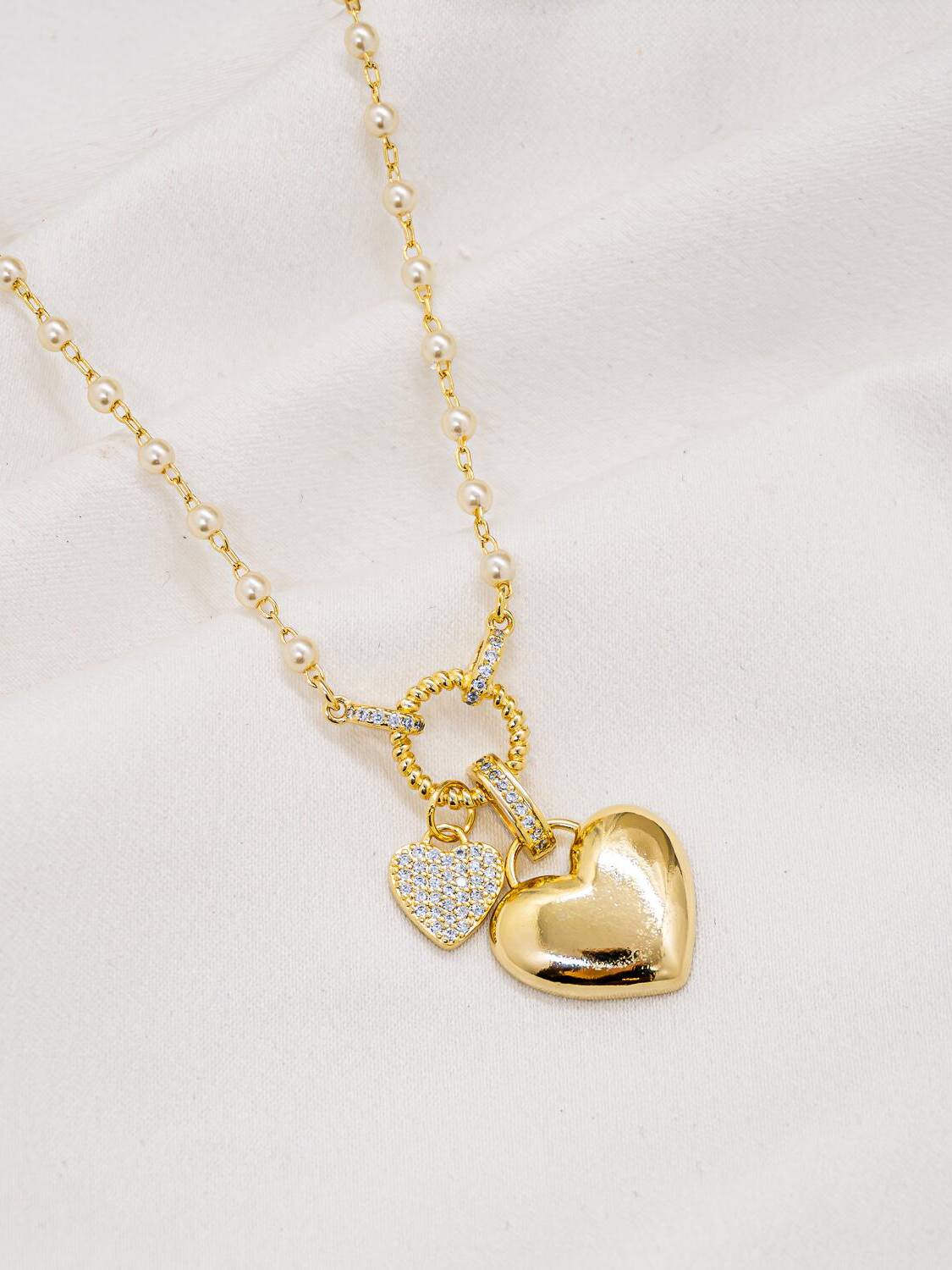 Collier doré à petites perles blanches, anneau torsadé et deux cœurs, l’un lisse, l’autre serti