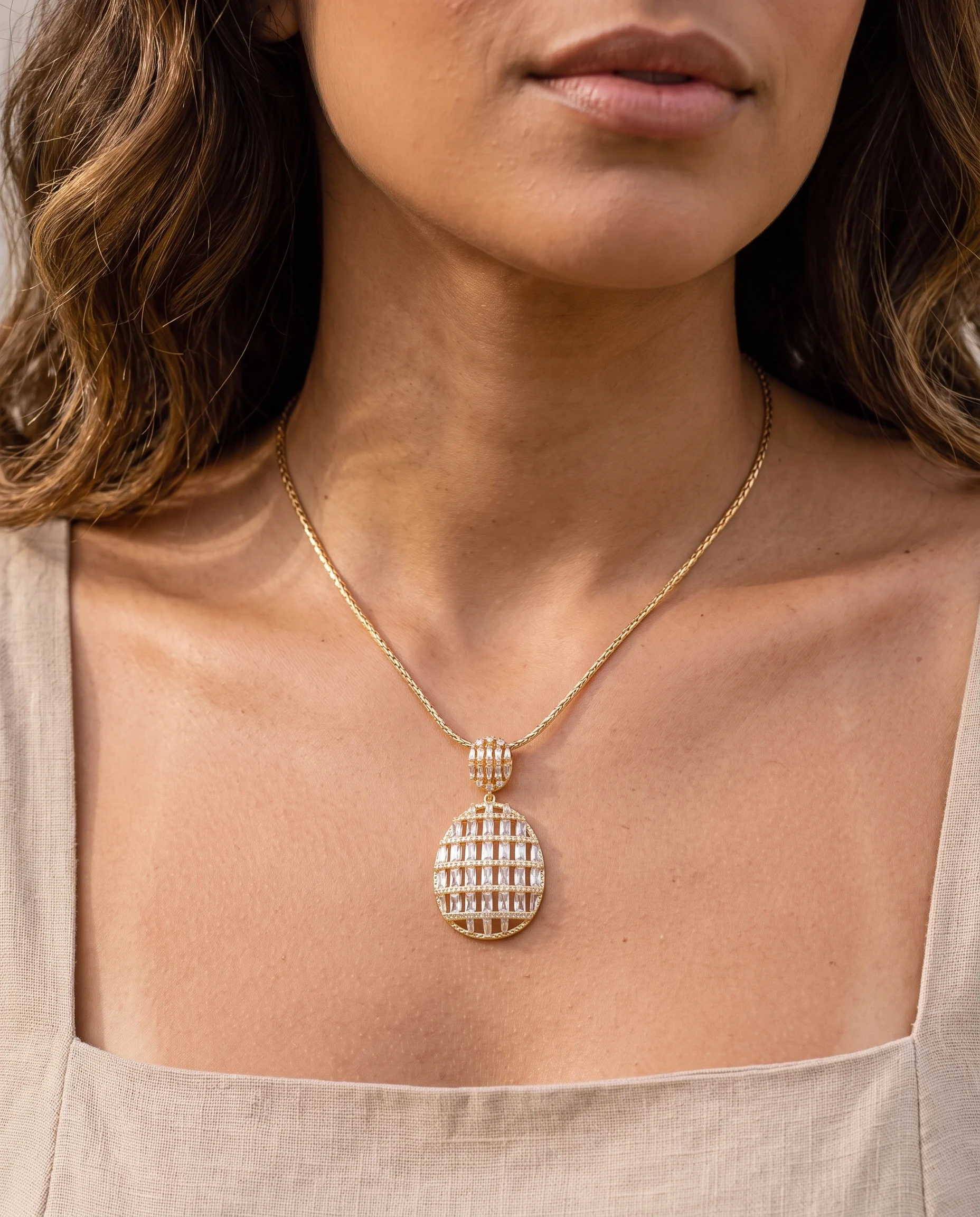 Collier doré à pendentif ovale ajouré serti de zircons baguette, porté sur la poitrine, vu de près