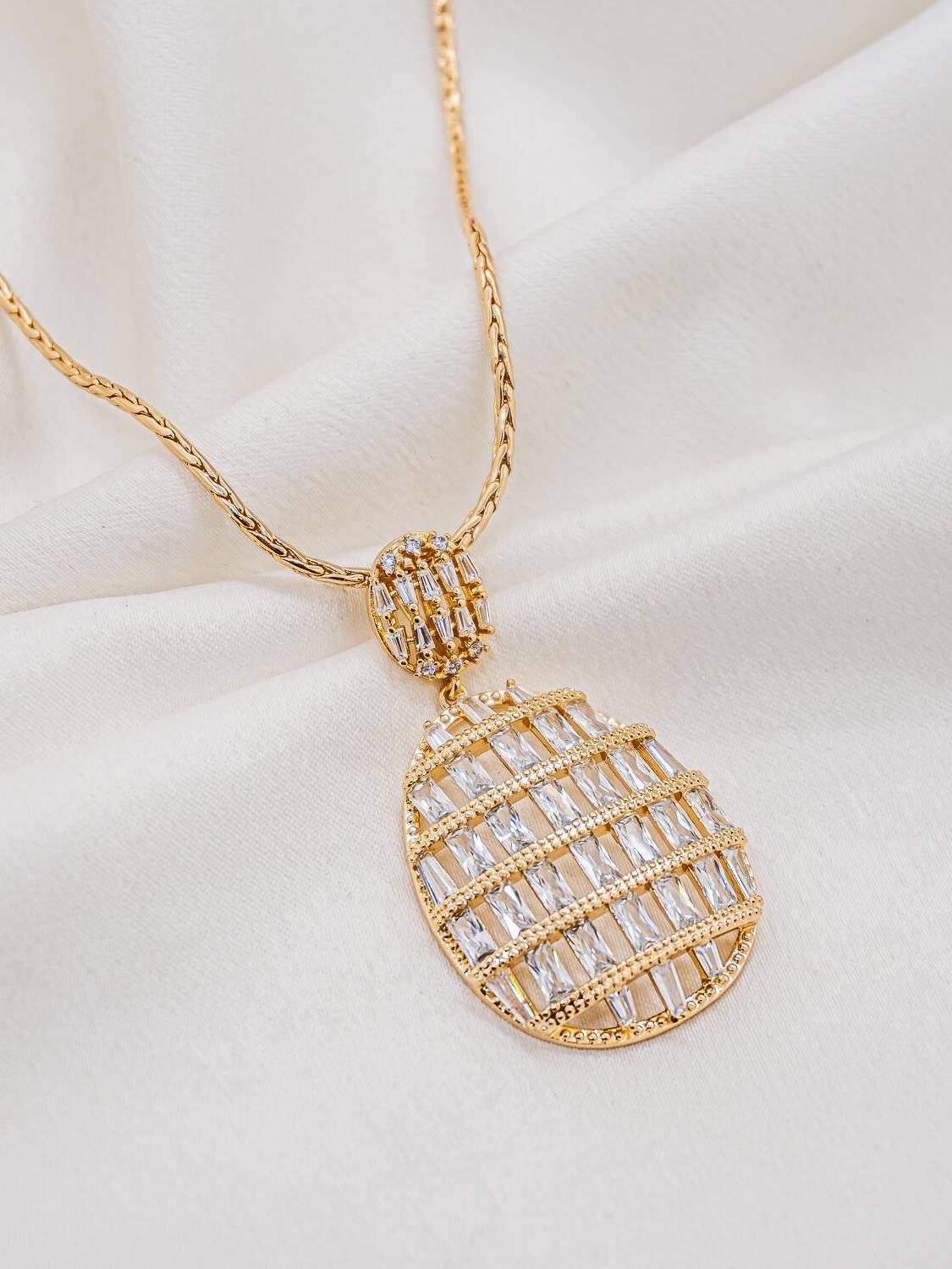Collier doré à long pendentif ovale ajouré, rangs de zircons baguette et passant serti
