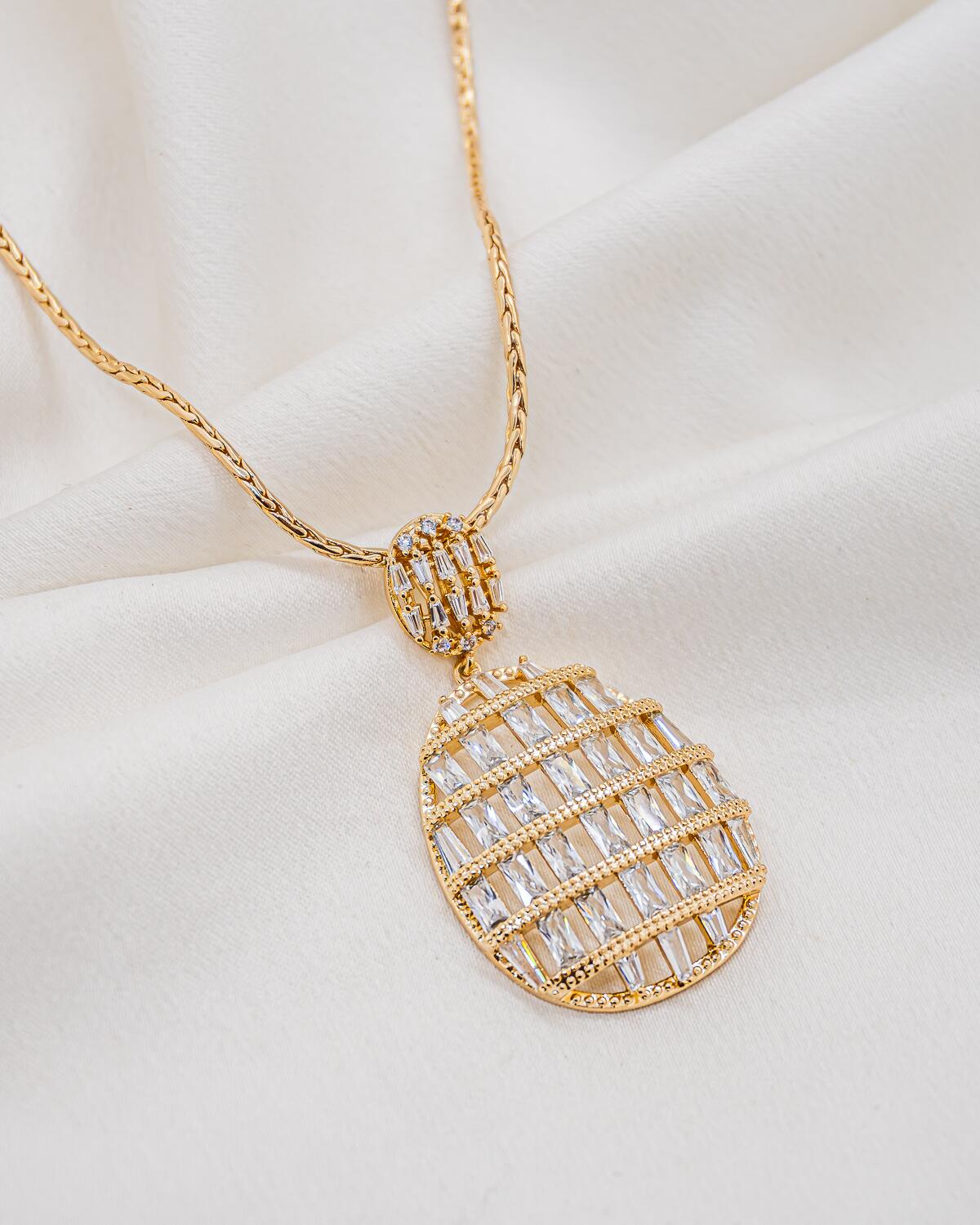 Collier doré à long pendentif ovale ajouré, rangs de zircons baguette et passant serti