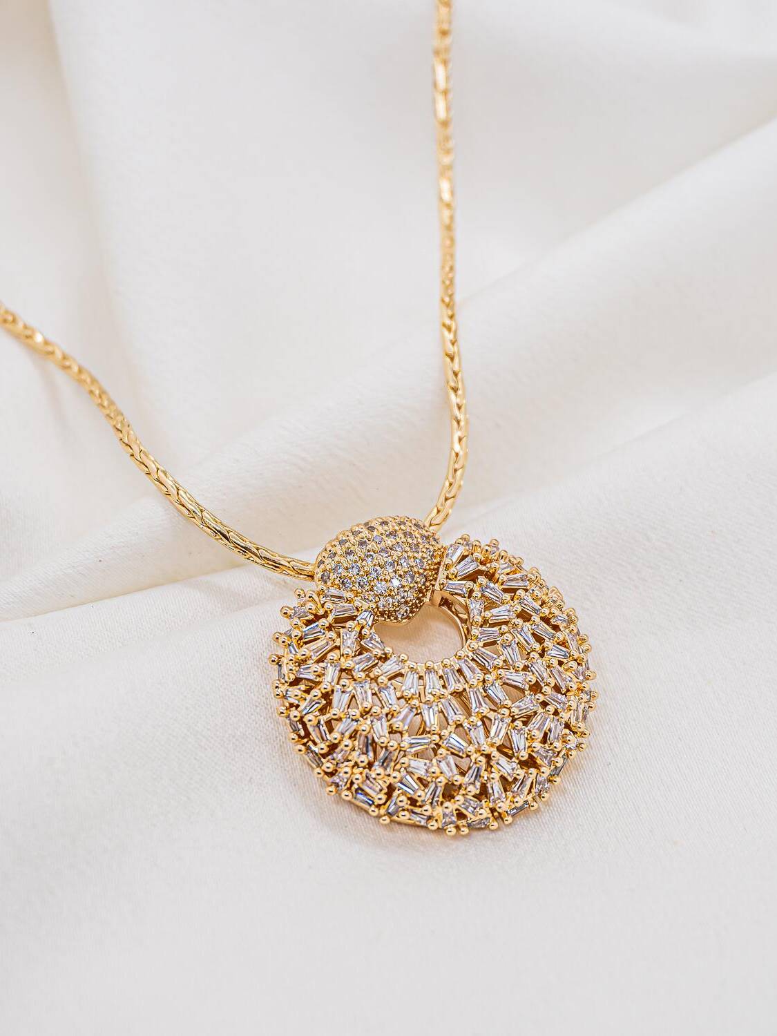 Collier doré à large pendentif rond ajouré couvert de zircons baguette, bélière en dôme sertie