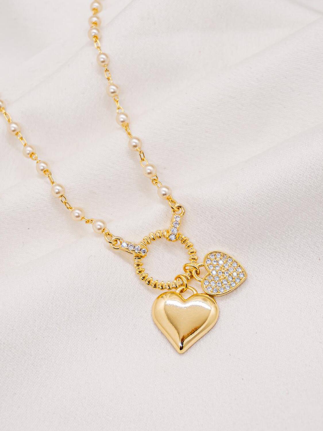 Collier doré de petites perles blanches avec anneau côtelé et deux cœurs, lisse et serti