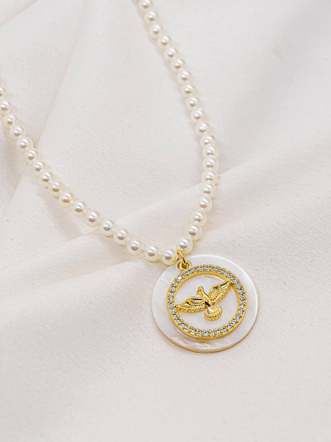 Collier de perles blanches et disque de nacre portant une colombe dorée cerclée de pierres