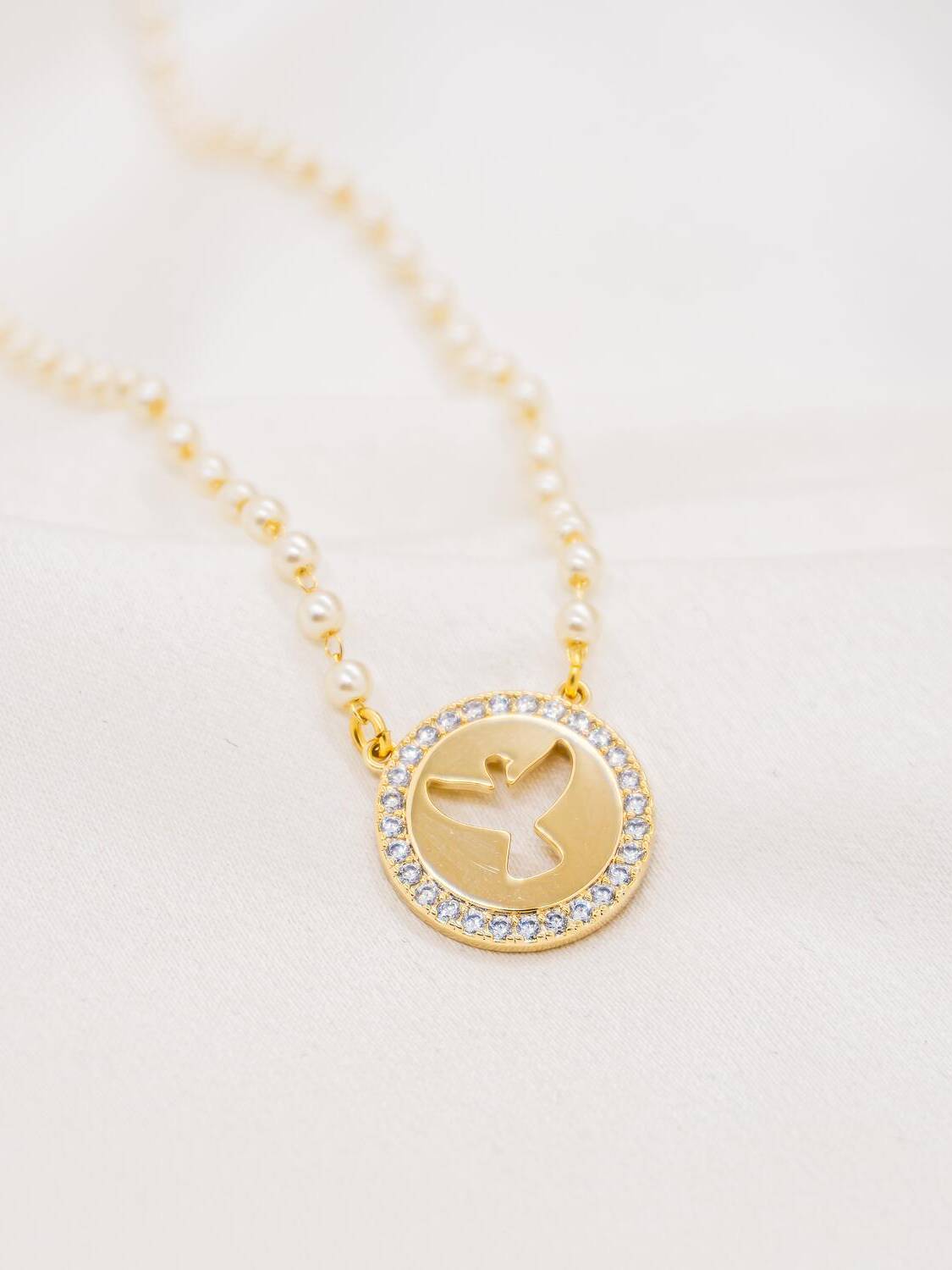 Collier de petites perles blanches avec médaille ronde dorée à colombe ajourée, bordée de pierres claires