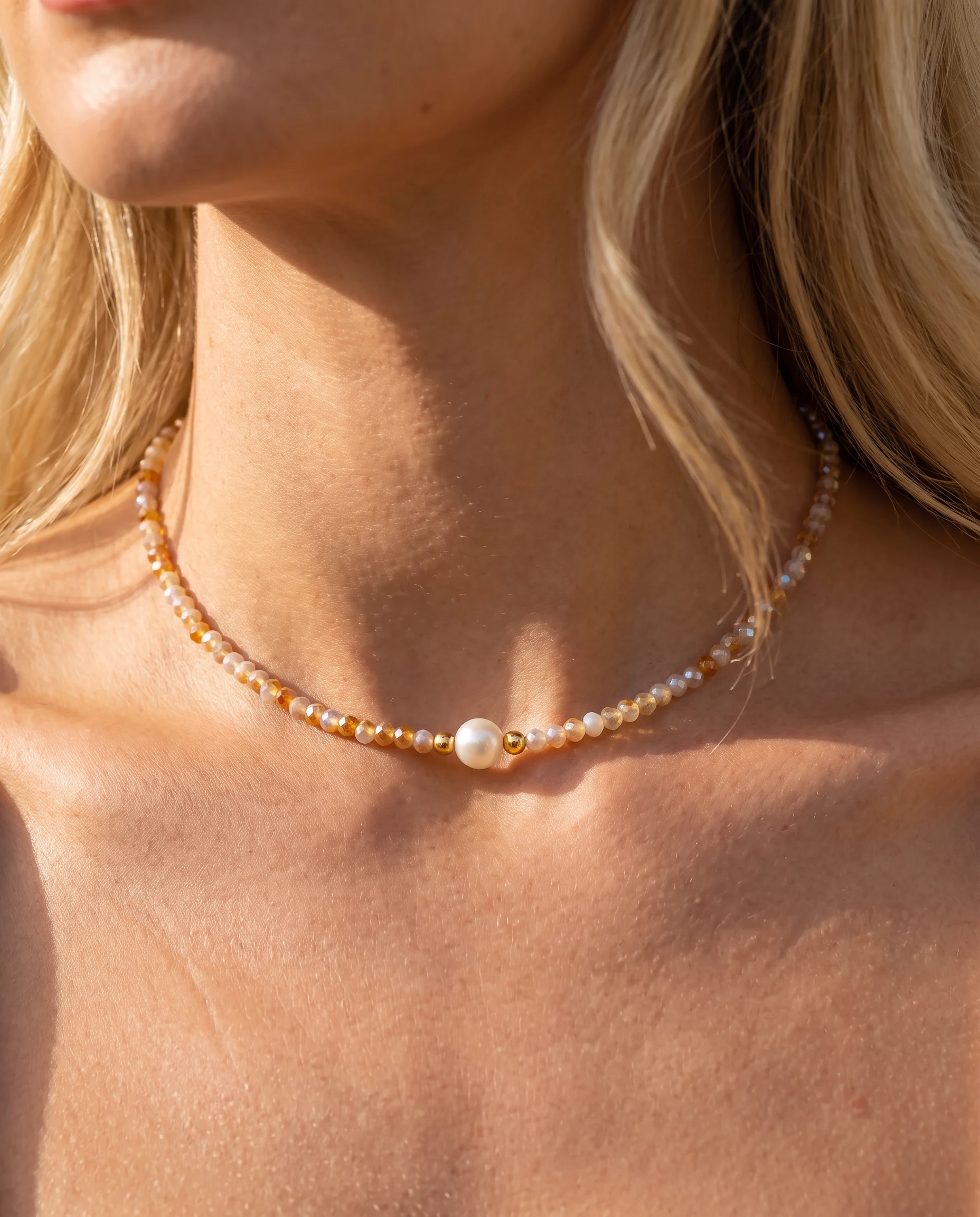 Choker necklace of small faceted beige and honey beads with a central white pearl, close-up view