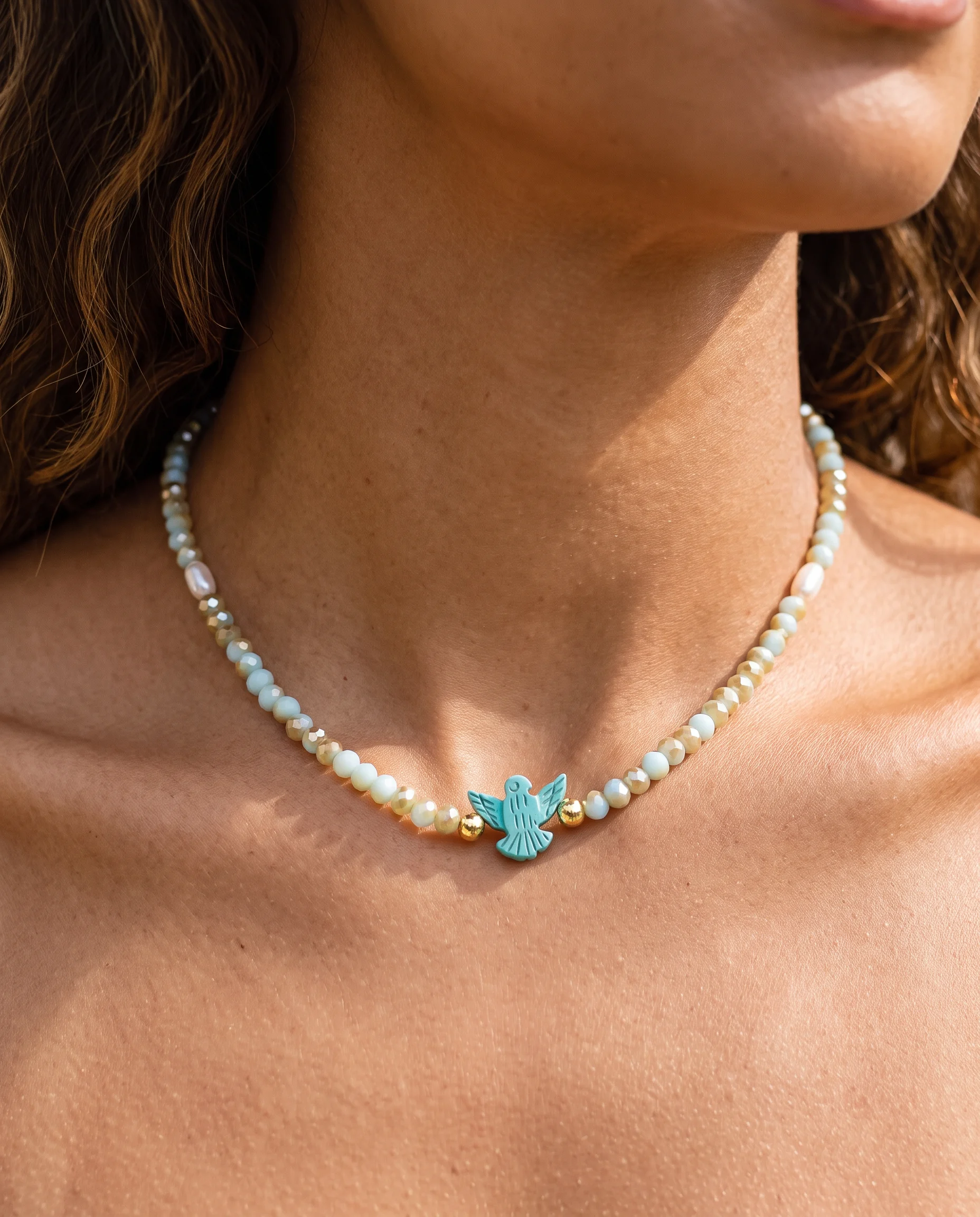 Ras-de-cou de perles facettées bleu pâle et dorées avec une petite colombe turquoise, vu de près