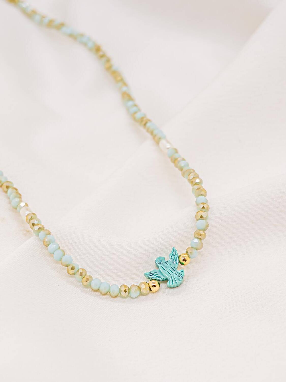 Ras-de-cou de cristaux facettés bleu pâle et dorés avec petite colombe turquoise au centre