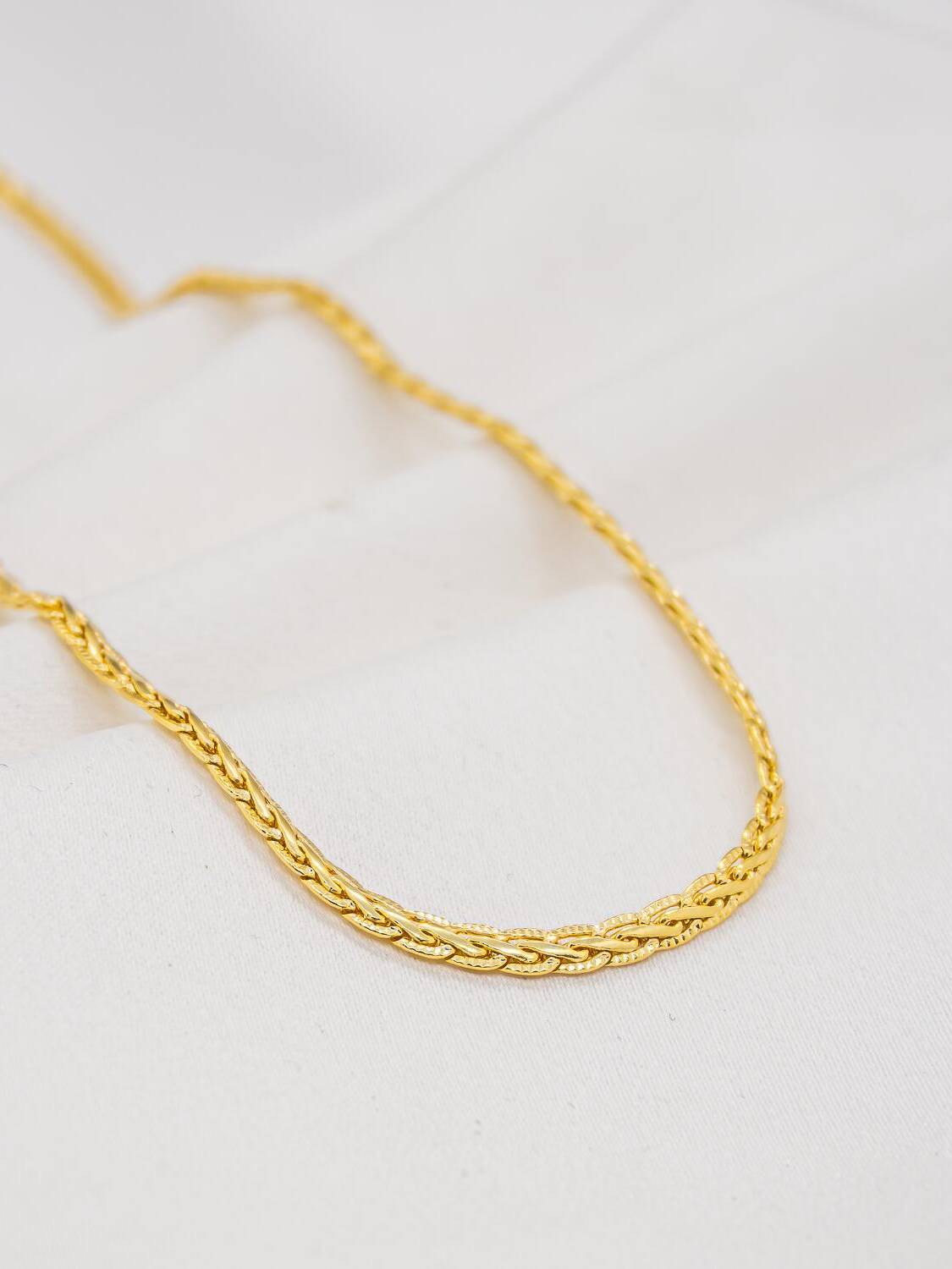 Ras-de-cou doré en maille natte plate entrelacée, finement striée, posé sur un tissu blanc