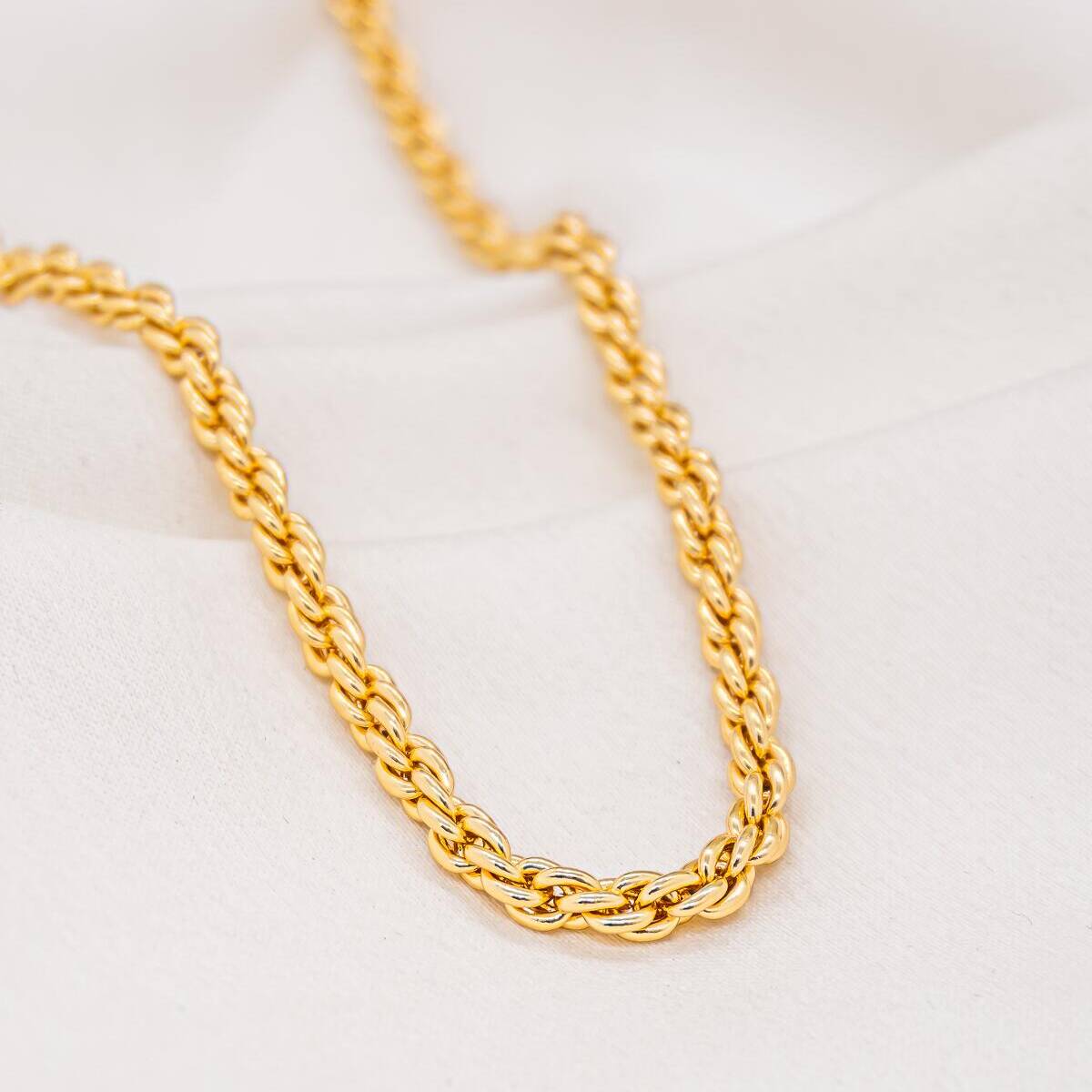 Gold choker necklace in thick, shiny twisted link, interlaced double links, on white fabric