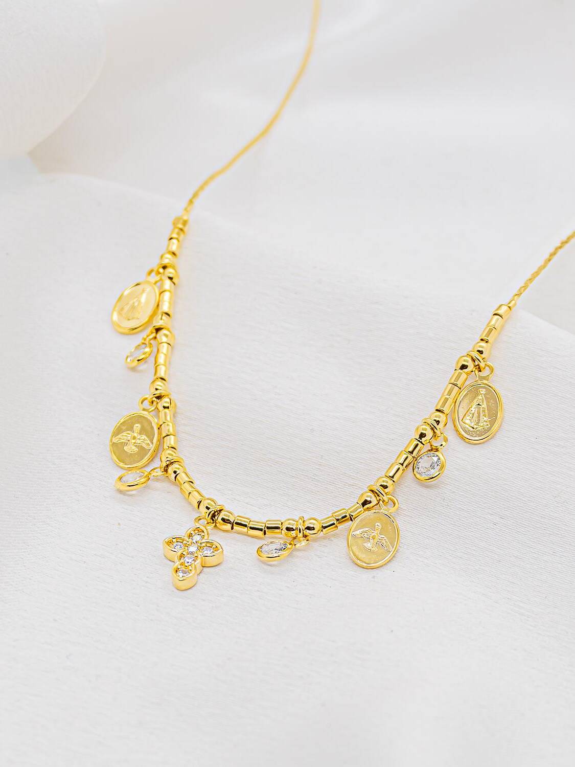 Collier ras-de-cou doré à petits tubes, médailles religieuses ovales, pierres claires pendantes et croix sertie