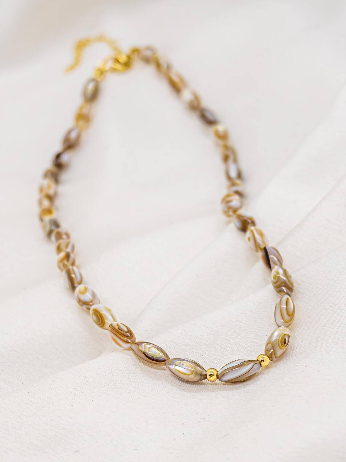 Ras-de-cou de perles ovales de nacre caramel et deux billes dorées sur tissu écru