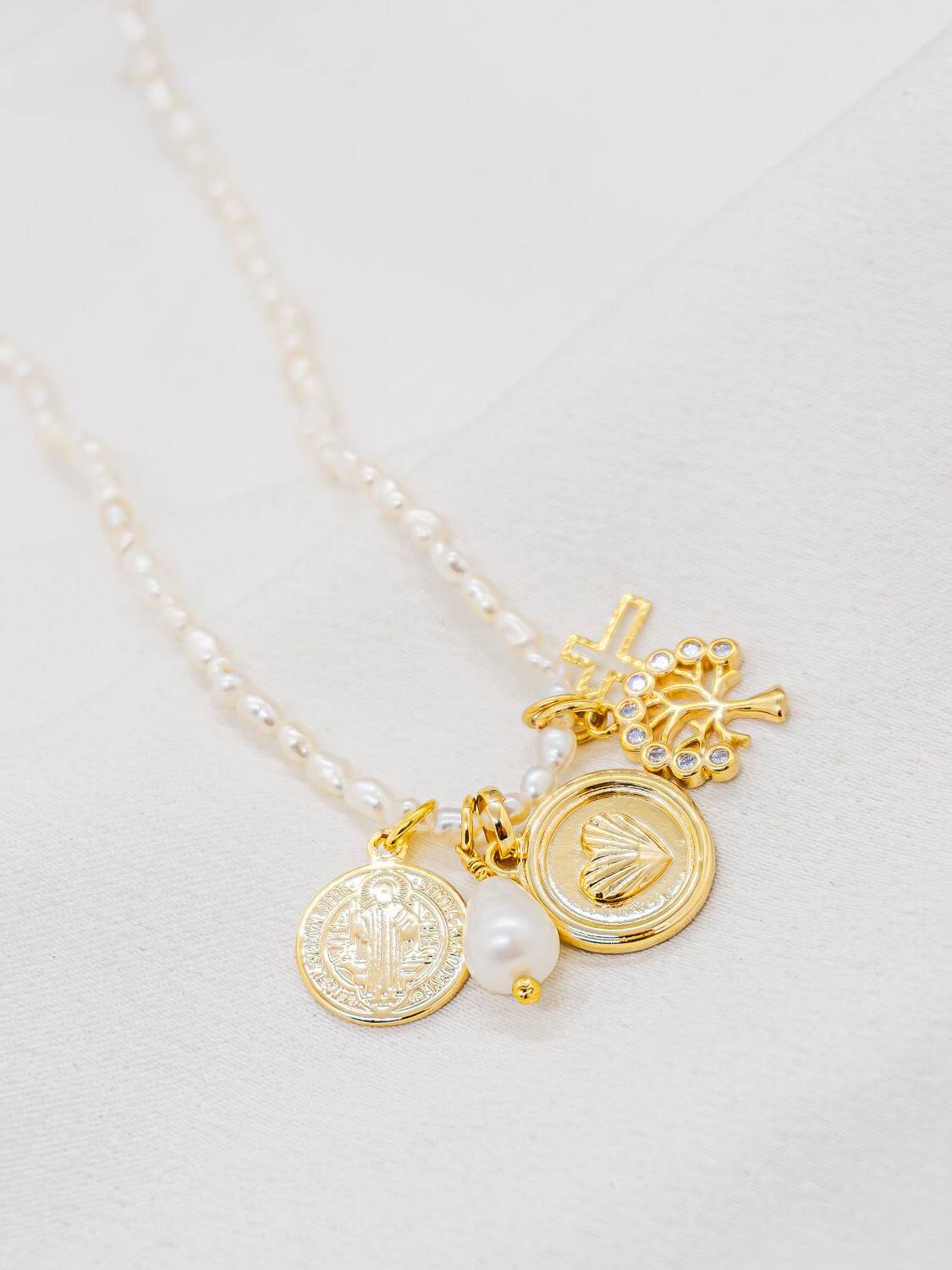 Collier de petites perles blanches avec breloques dorées : médailles, croix, motif serti, perle en goutte