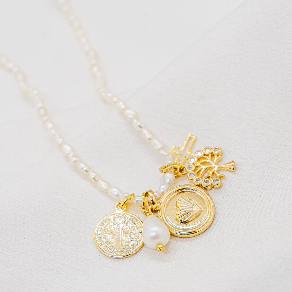 Small white pearl necklace with golden charms: medals, crosses, pavé-set motif, teardrop pearl