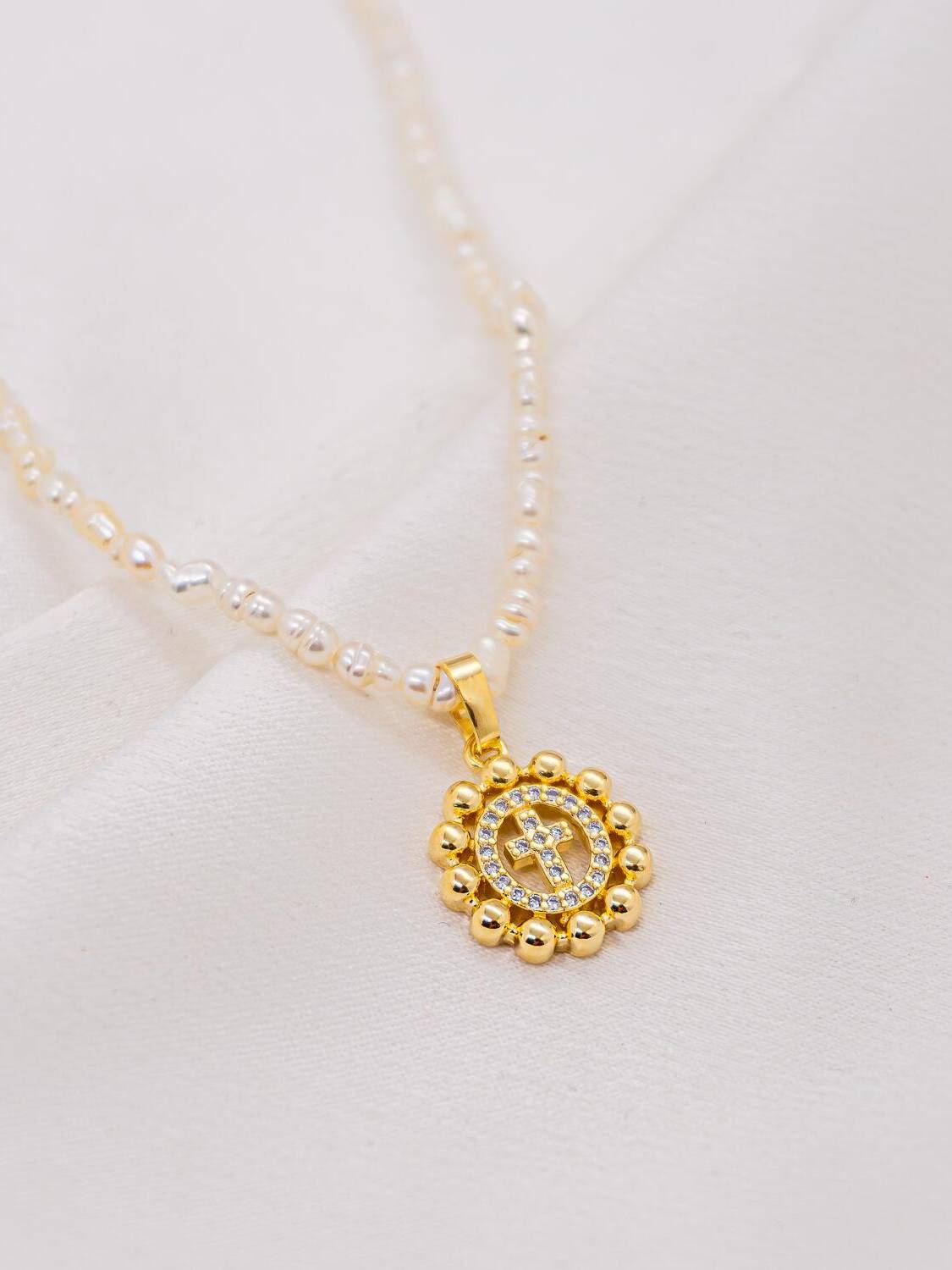 Ras-de-cou de petites perles irrégulières avec petite médaille ronde dorée à croix sertie de pierres claires